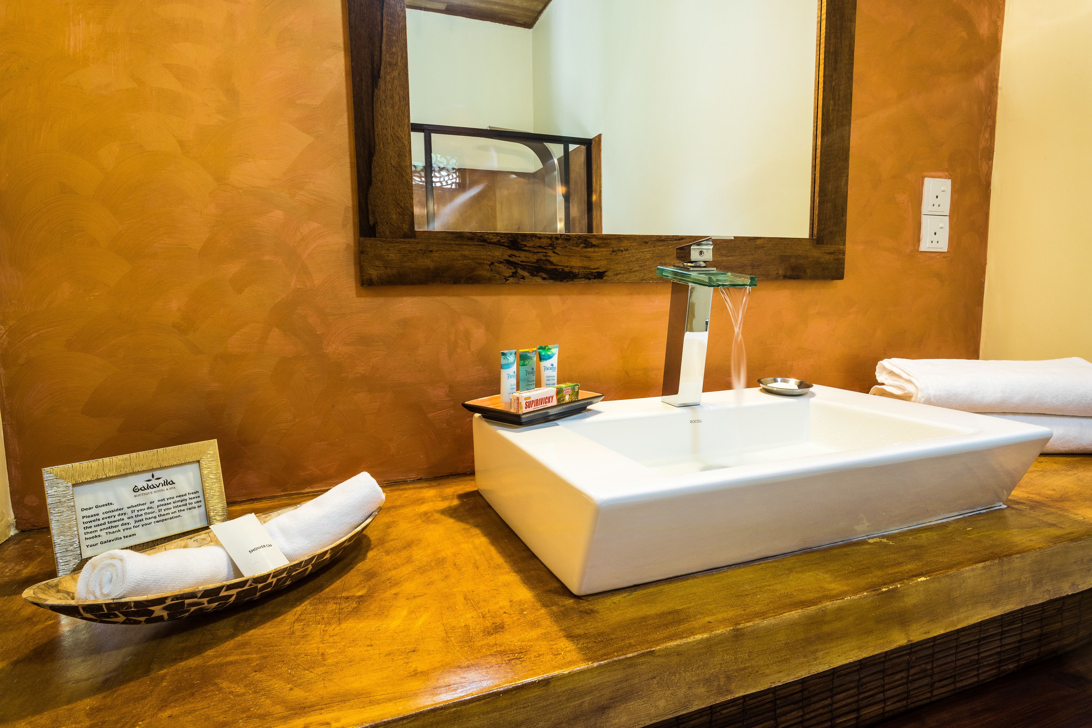 A bathroom with a white sink, a mirror, and toiletries in a tray.