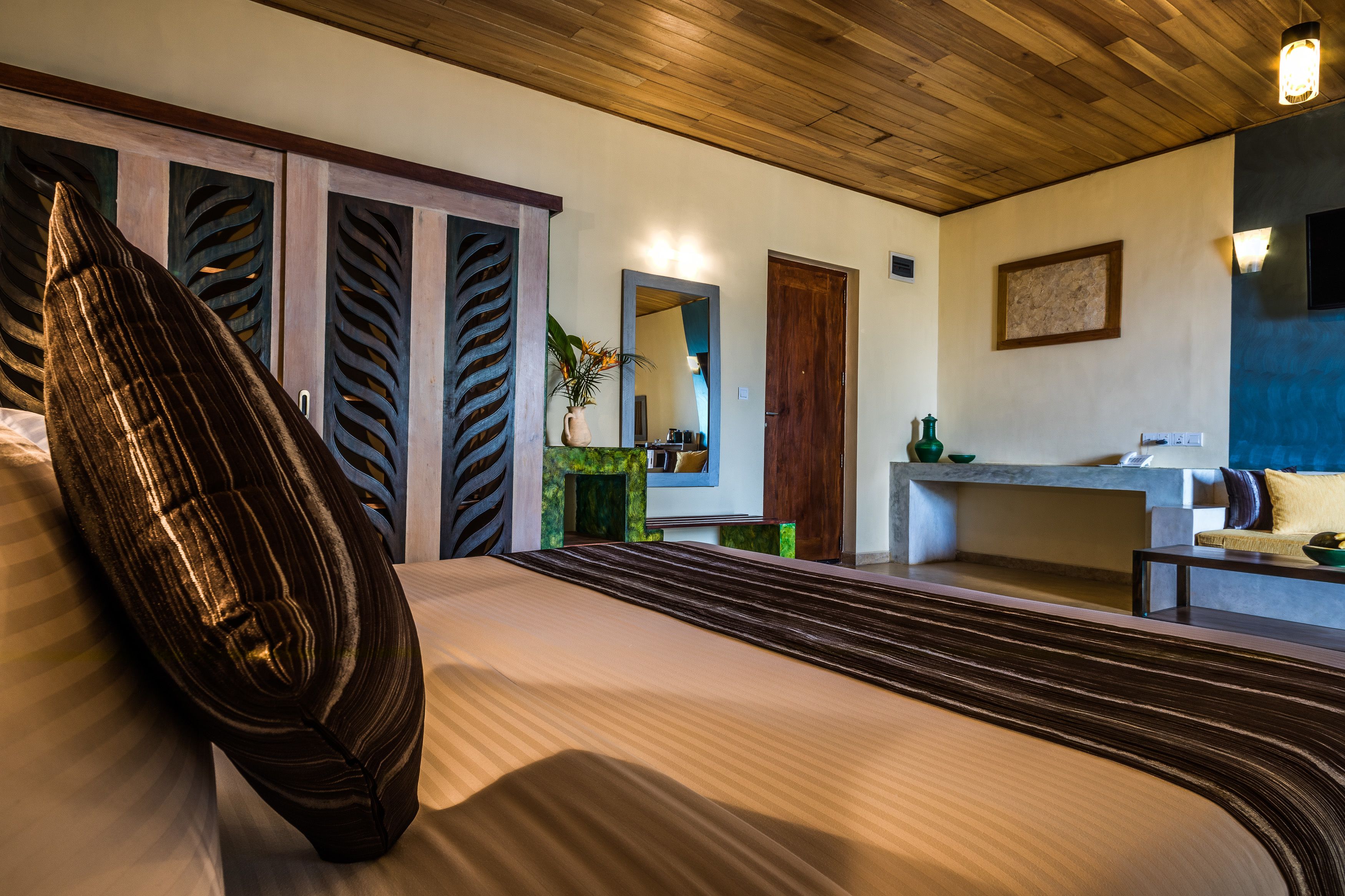 A bedroom with a large bed, wooden ceiling, and a view of a bathroom with a sink and mirror.