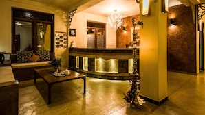 Un vestíbulo con mostrador de recepción, candelabro, sofá con cojines estampados y una mesa baja con una bandeja de objetos.