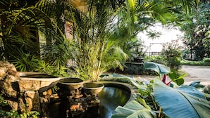 Un jardín con un estanque, estructuras de piedra y plantas tropicales.