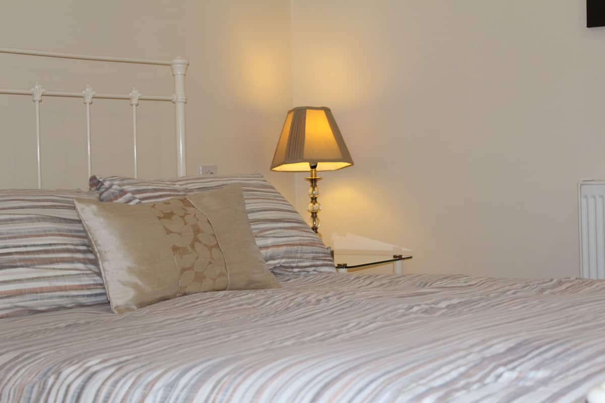 Una cama bien hecha con ropa de cama a rayas, una lámpara de noche y un radiador.