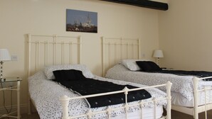 A room with two beds, each with a white frame and a black headboard, a small bedside table with a lamp, and a wall-mounted picture of a cityscape. - The Bulls Head (Chichester)