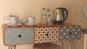 A small wooden table with a patterned cabinet, a kettle, two water bottles, a glass, and a cup. - The Bulls Head (Chichester)
