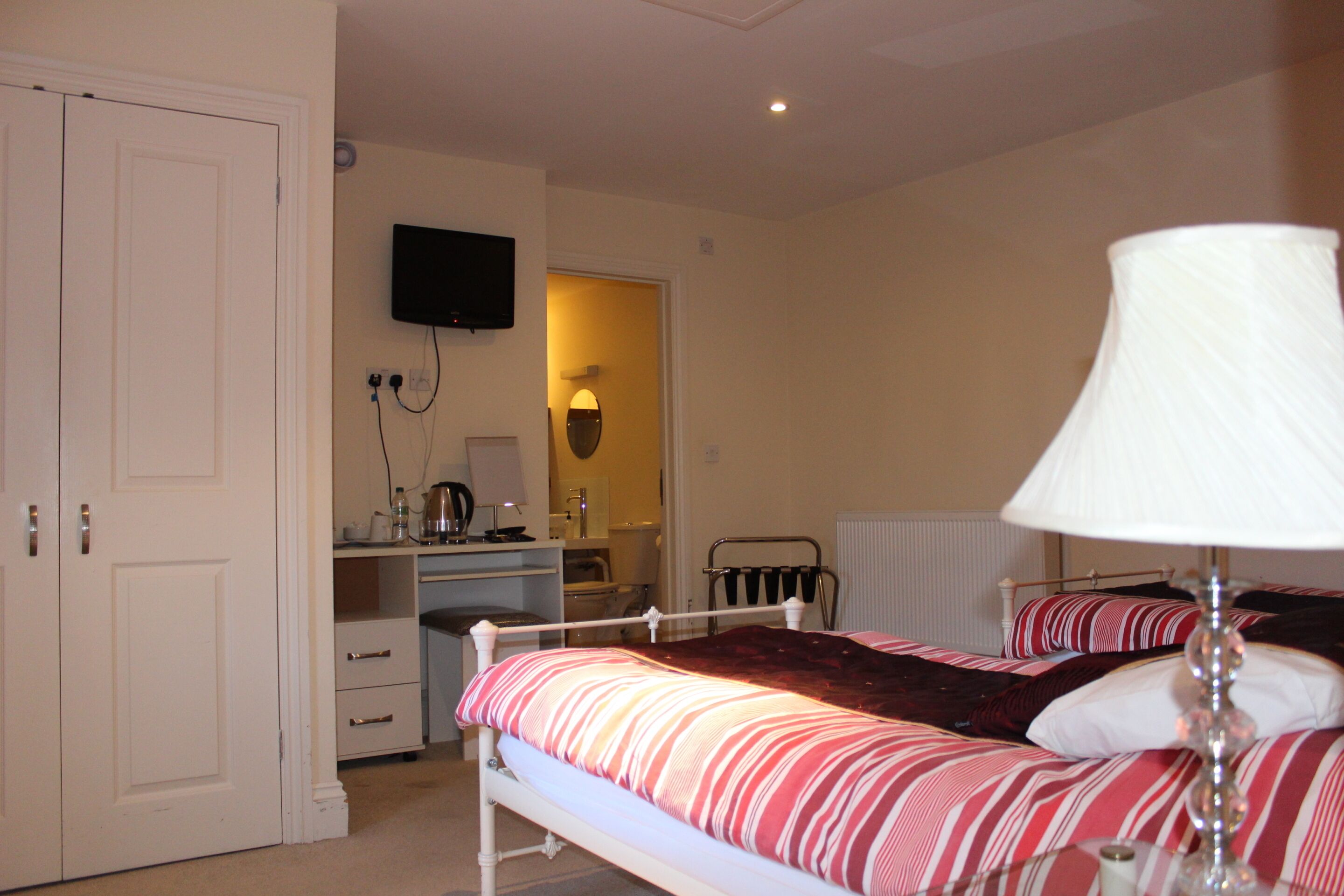 A bedroom with a bed, bedside table, lamp, and a TV mounted on the wall.