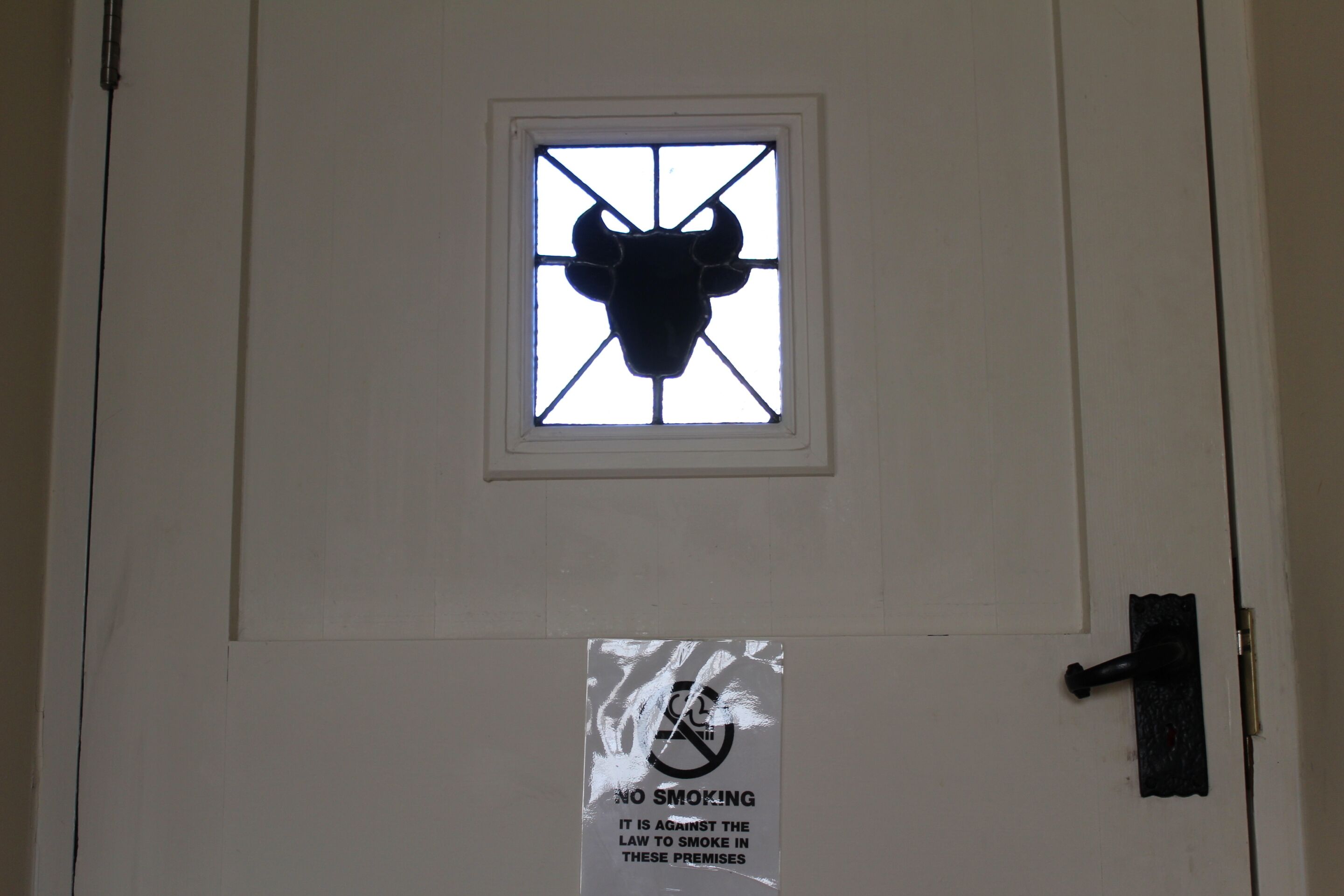 A door with a bull's head window and a no smoking sign.
