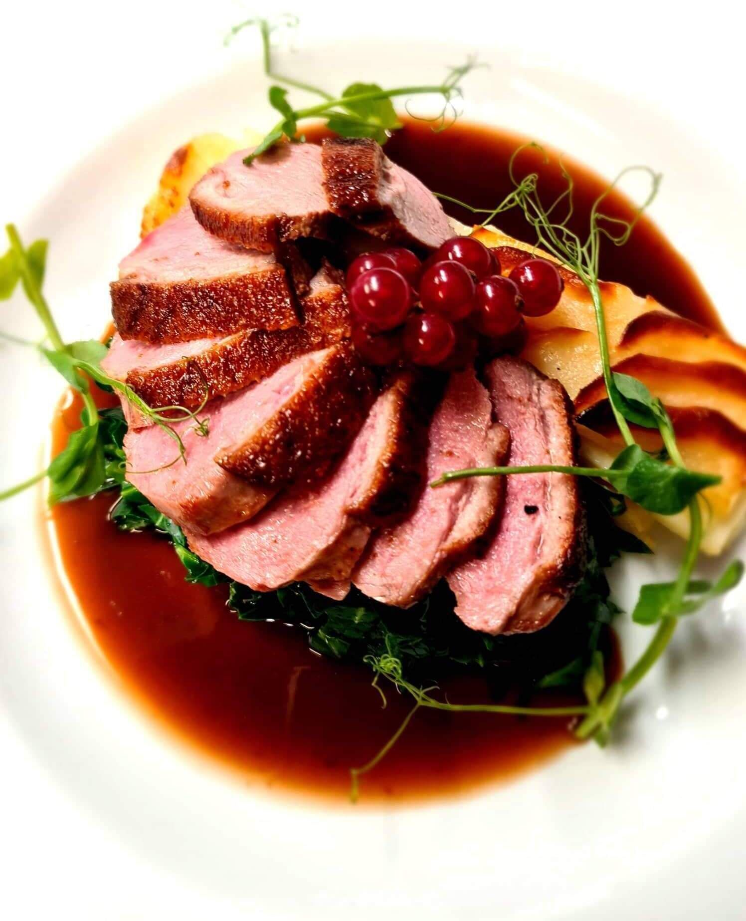 A dish with sliced meat, red berries, and greens on a plate.