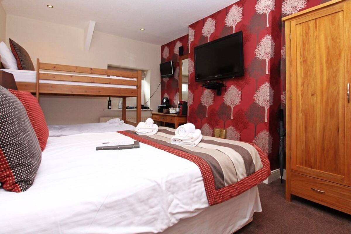 Een hotelkamer met een stapelbed, een wandtelevisie, een houten kledingkast en behangpapier met een rood-wit patroon.