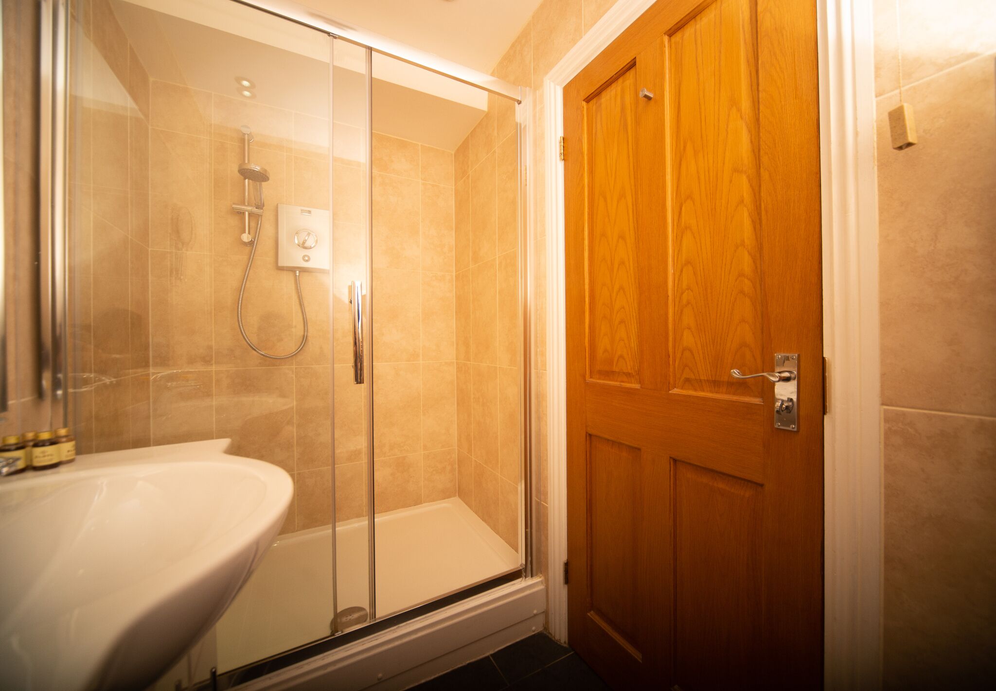 Un bagno con doccia vetrata, lavandino bianco e porta in legno.