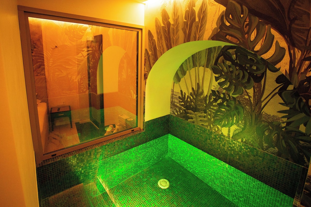 Une salle de bain dotée d’une paroi en verre, de carreaux de mosaïque verts et d’un mur végétal décoratif.