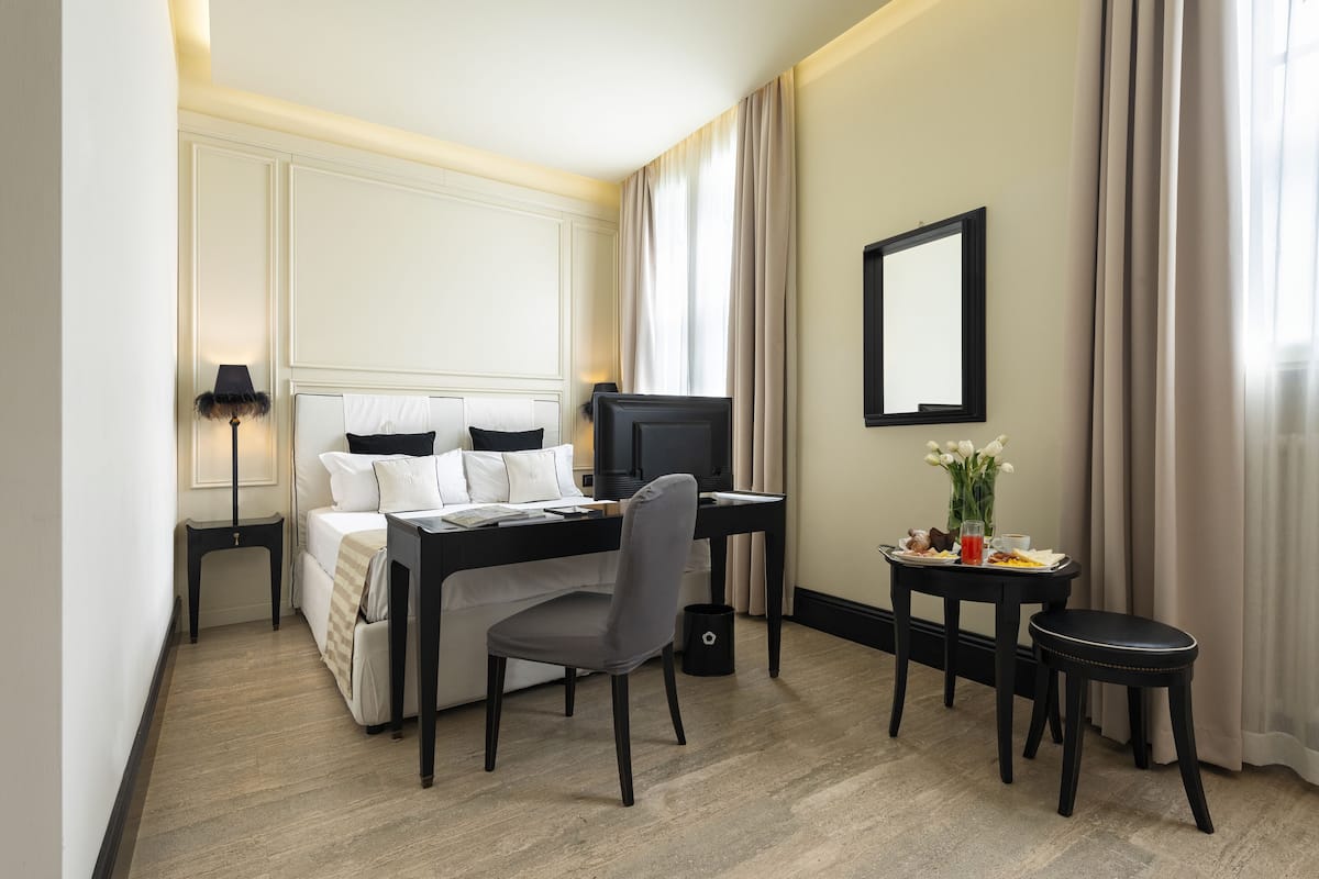 Une chambre d’hôtel avec un lit, un bureau, une chaise et une petite table sur laquelle est posé un vase de fleurs.
