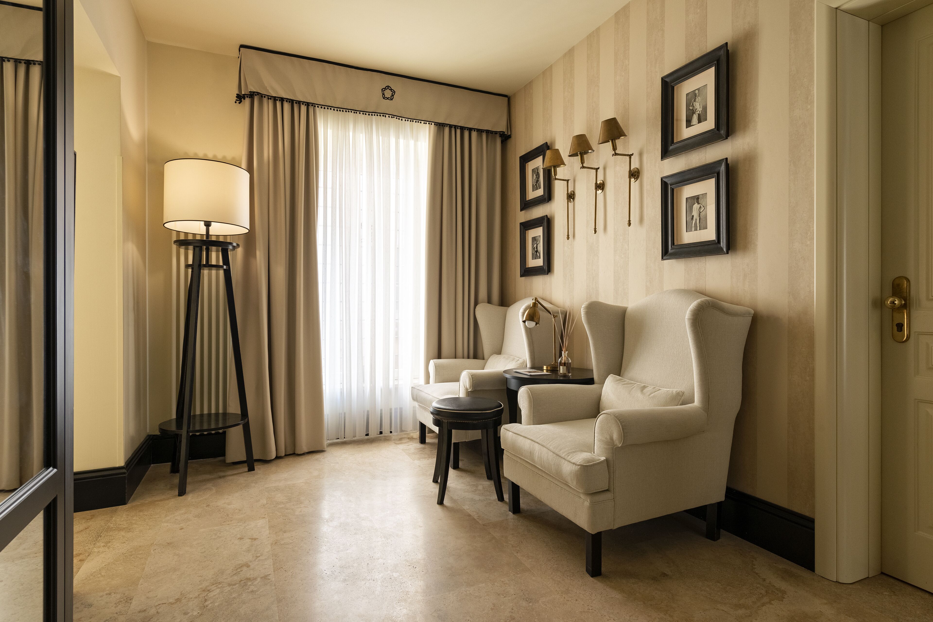 A hotel room with a large window, two armchairs, a floor lamp, and a small table.