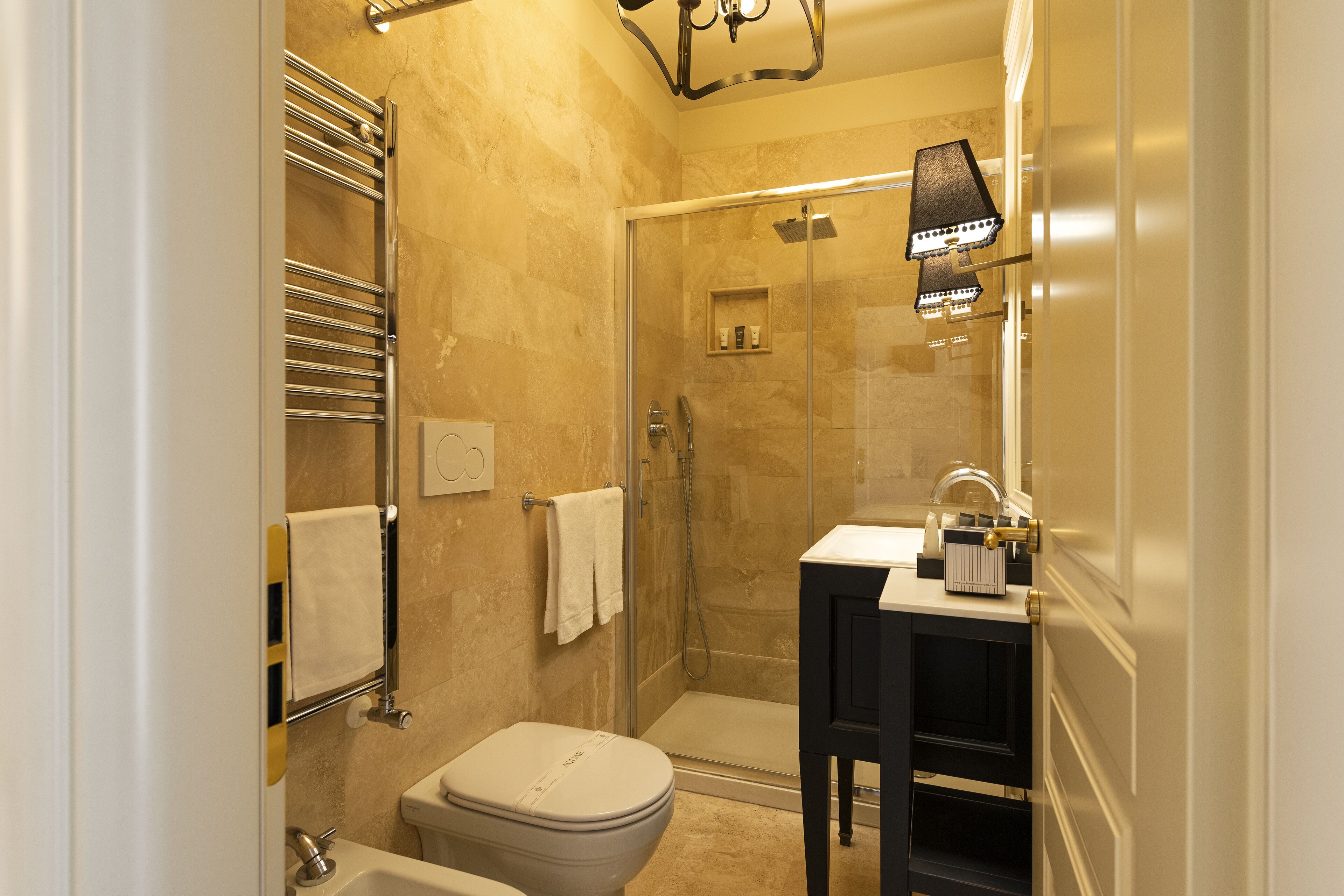 Un bagno con doccia vetro-muraria, un water, un lavabo con specchio e un porta asciugamani.