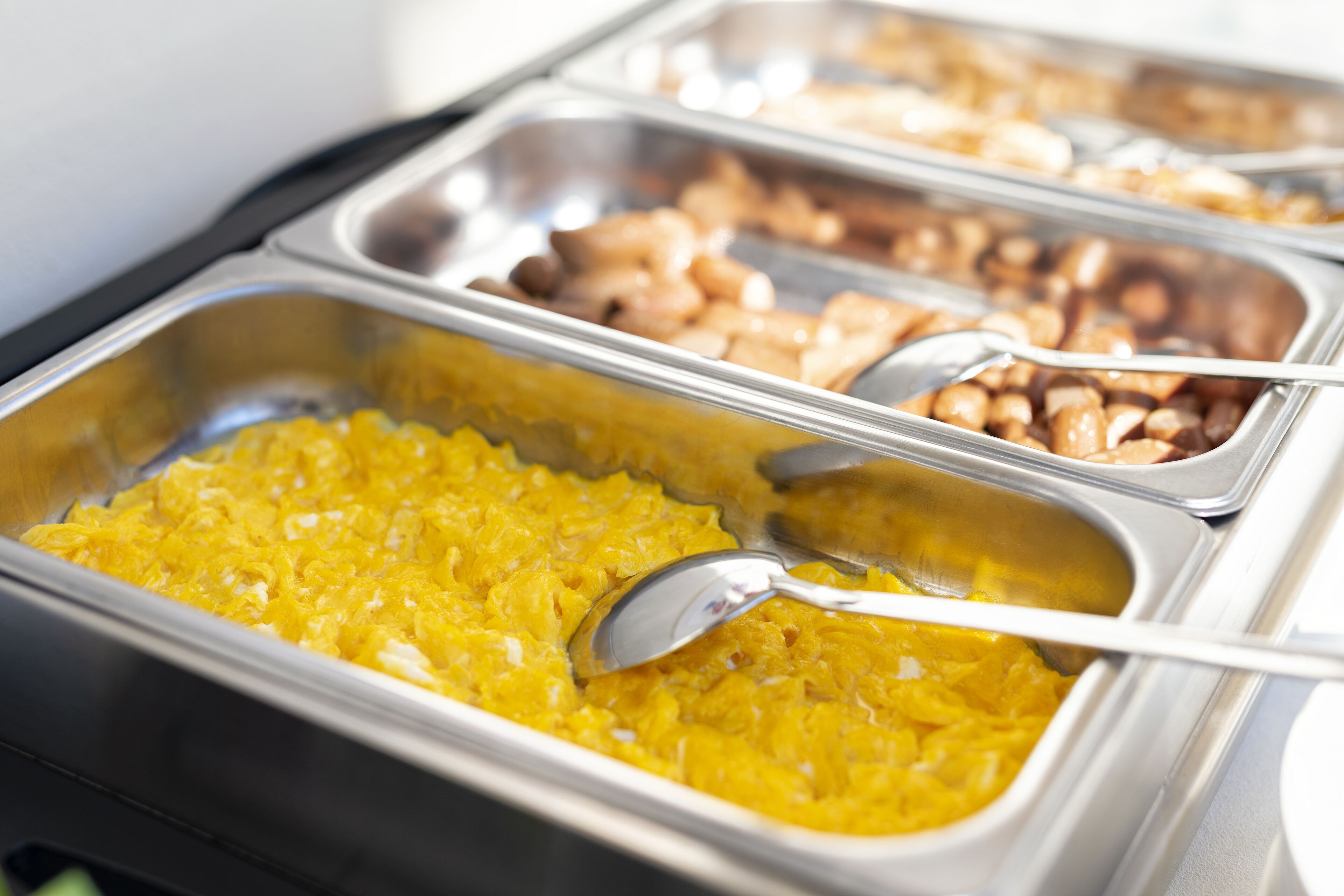 Un bufé con diversos alimentos en recipientes metálicos, incluyendo una sección con comida amarilla y otra con alimentos color café.