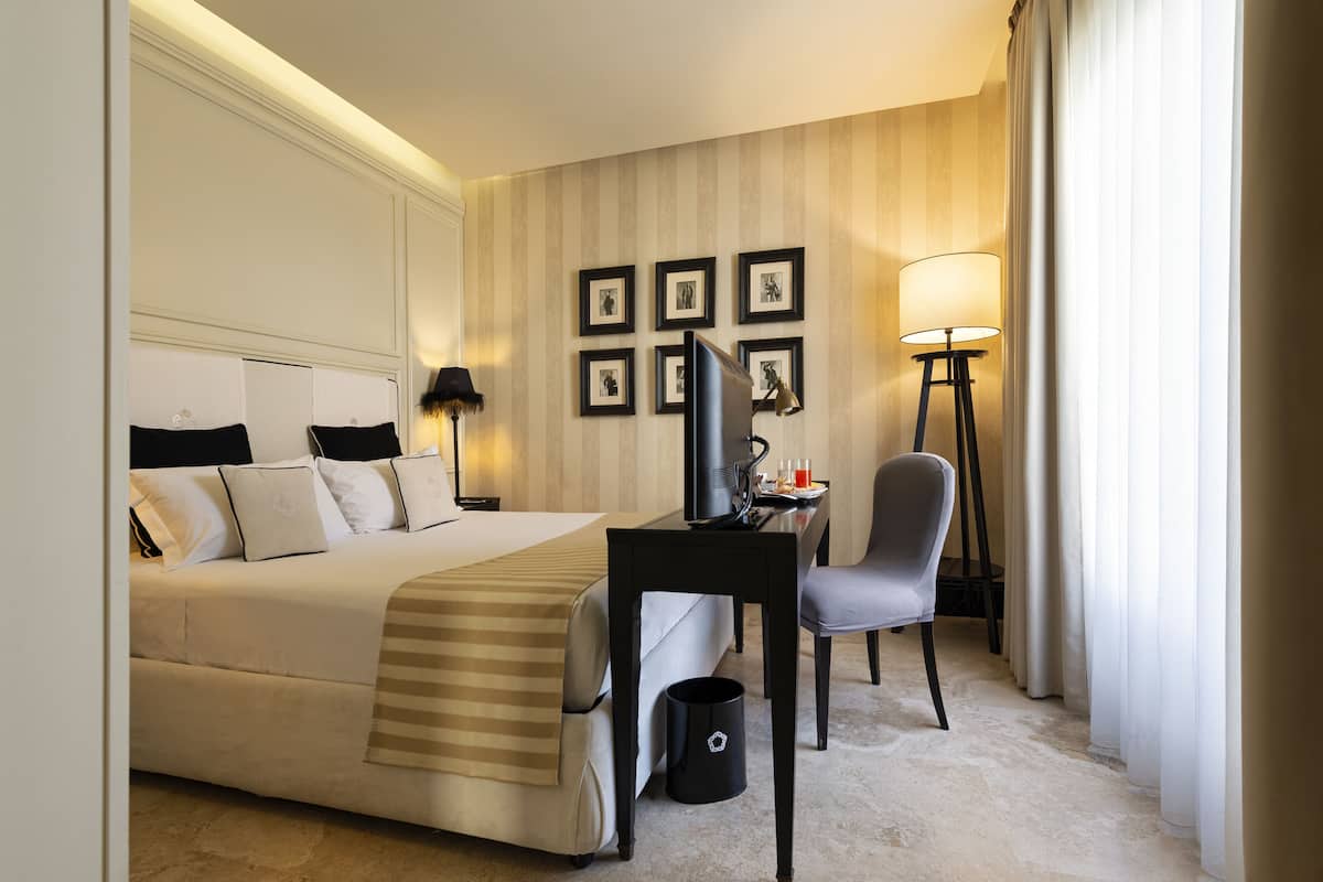 Une chambre d’hôtel avec un lit, un bureau, une chaise, une lampe et des tableaux encadrés au mur.