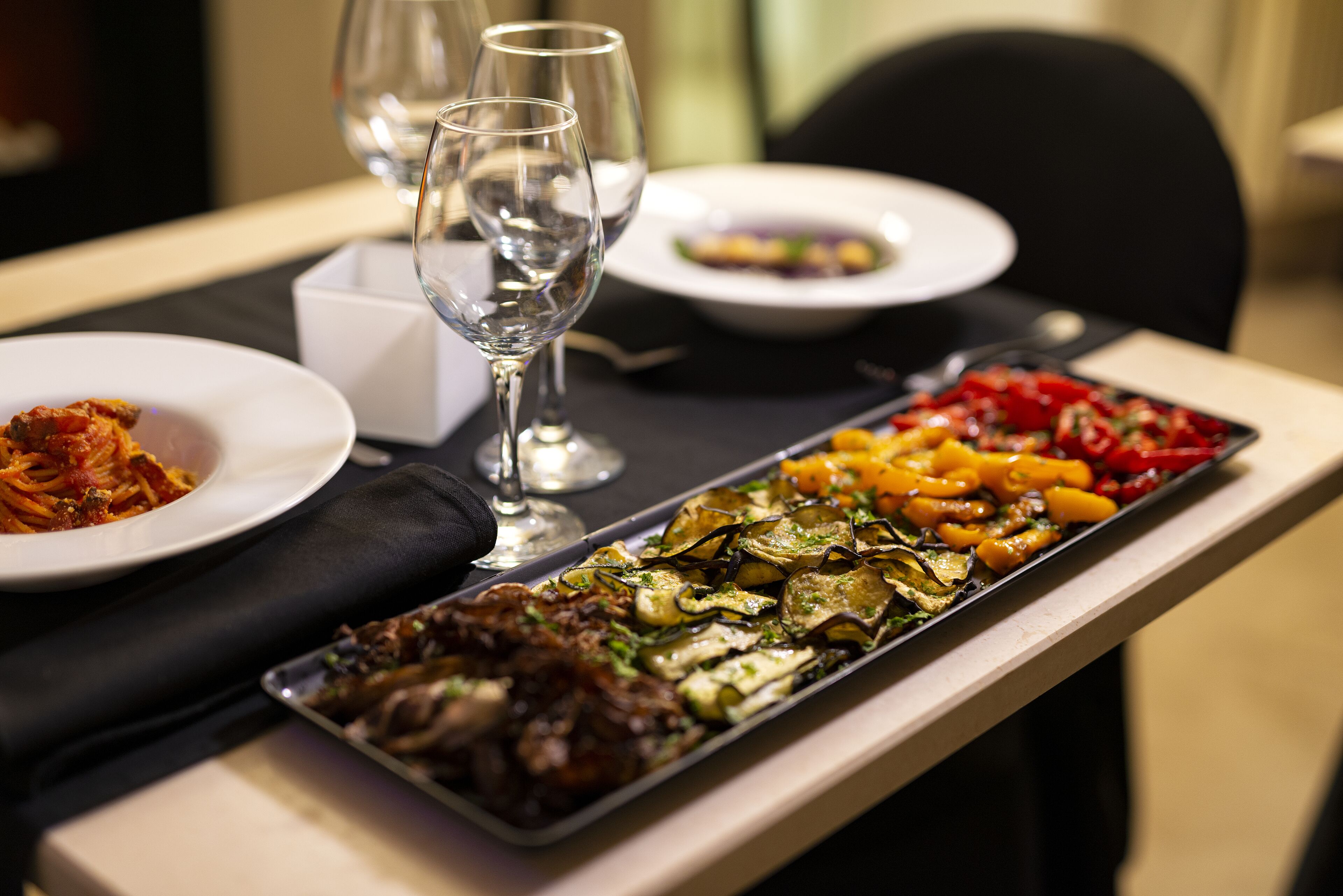 Uma mesa de jantar com diversos pratos, copos e uma bandeja de comida.