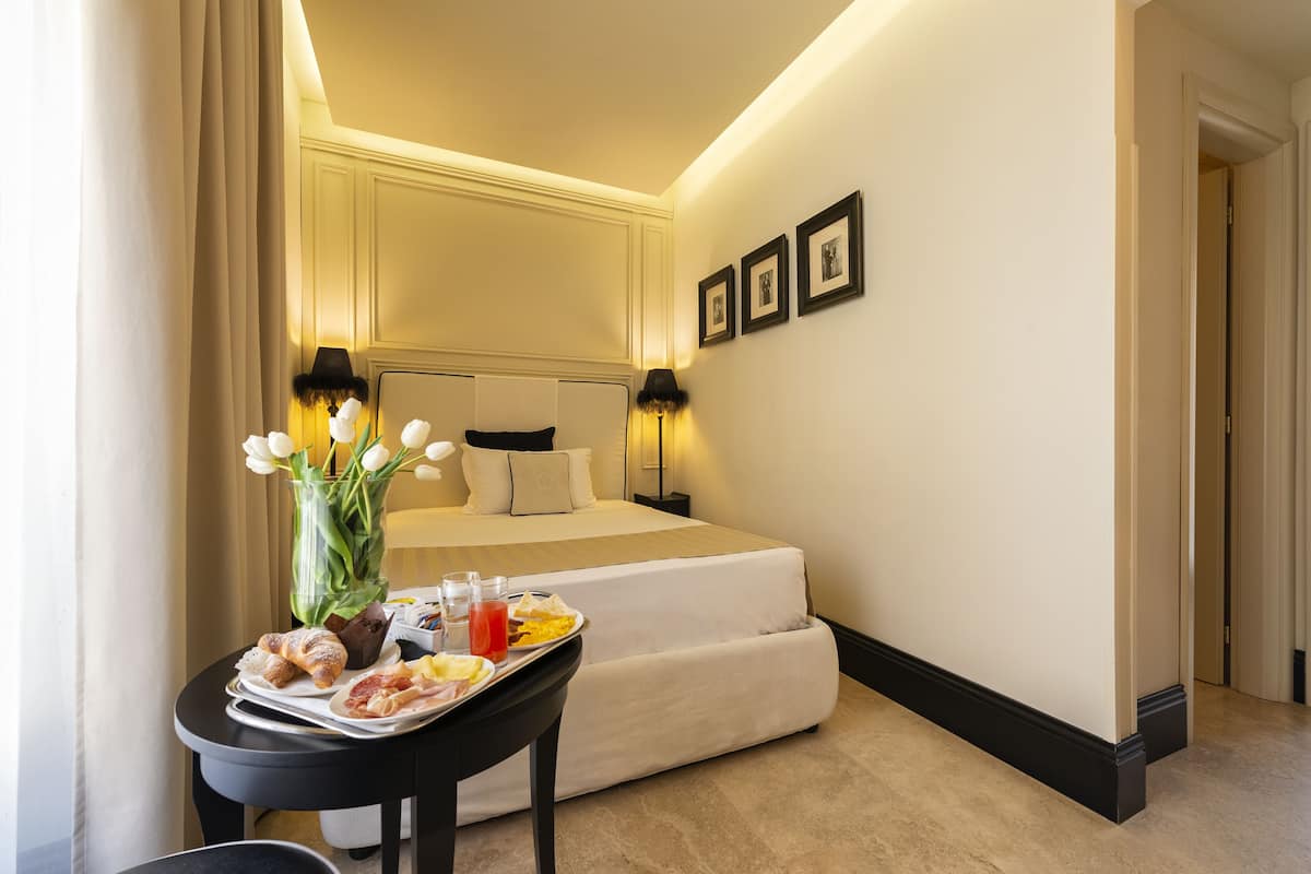 Une chambre d’hôtel avec un lit parfaitement fait, une table à manger où le petit-déjeuner est servi, et un vase rempli de fleurs.