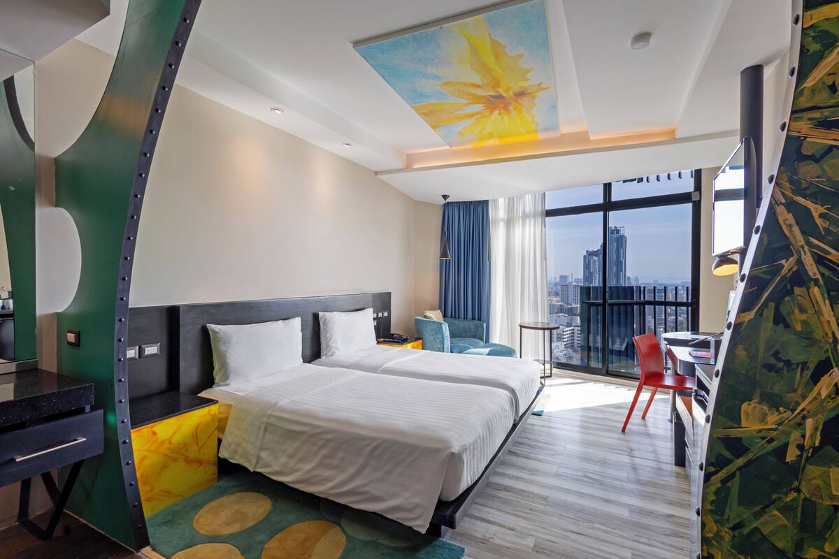 Habitación de hotel con dos camas, un escritorio, una silla, vistas a la ciudad y un diseño moderno de techo.
