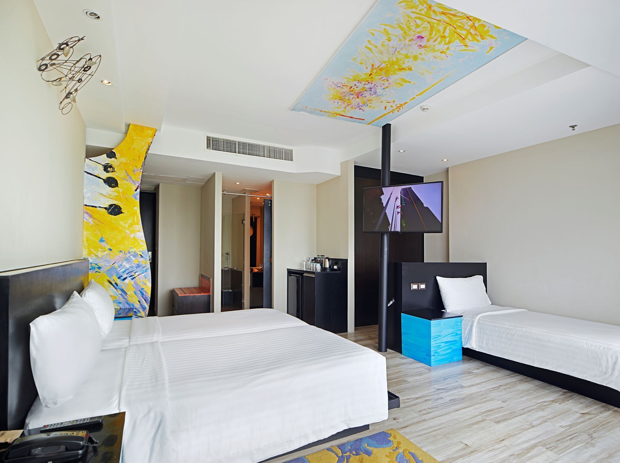 Habitación de hotel con dos camas, televisión y techo con diseño floral.
