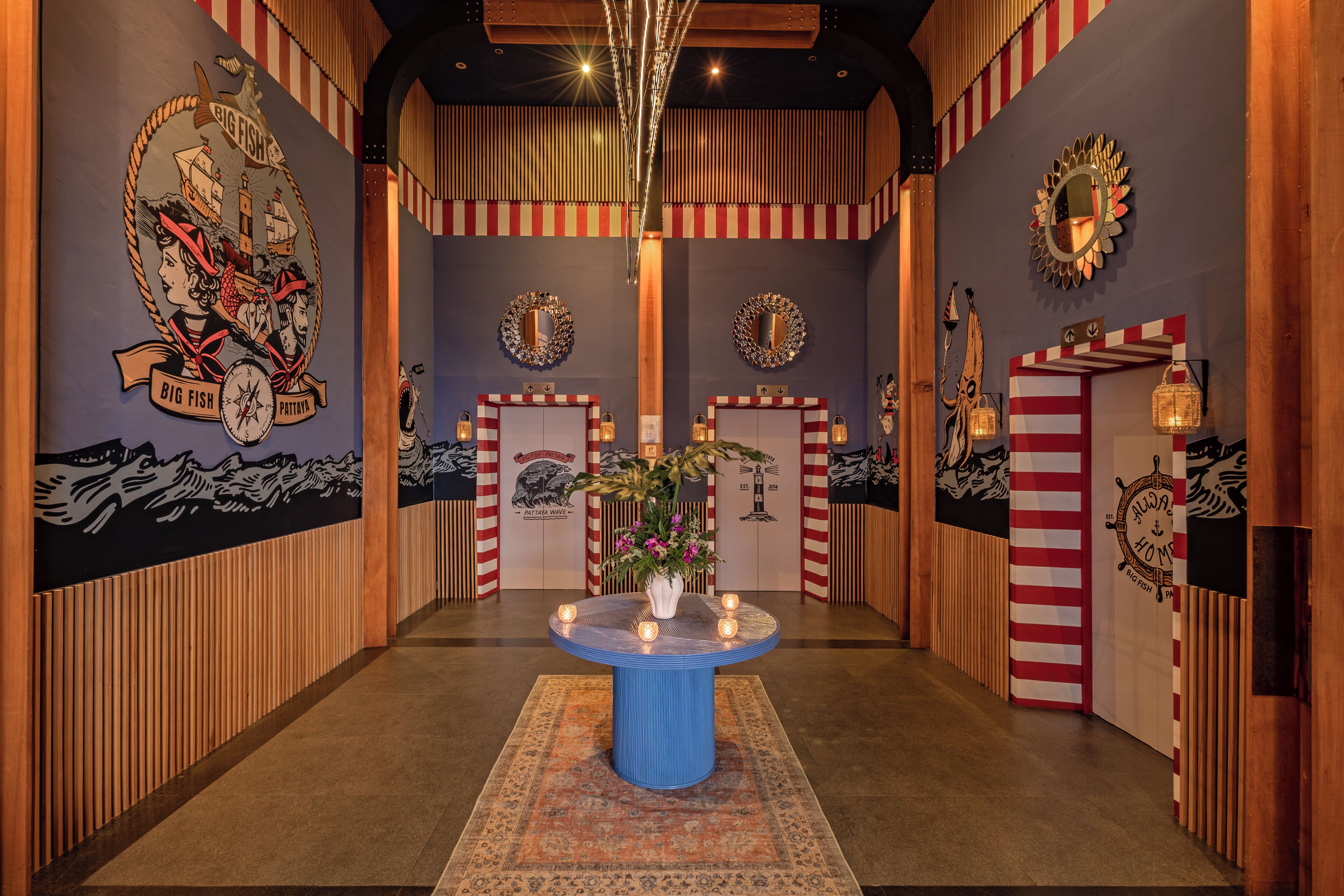 Een gang met gestreepte wanden, kunstwerken met een nautisch thema en een ronde tafel in het midden met een vaas.
