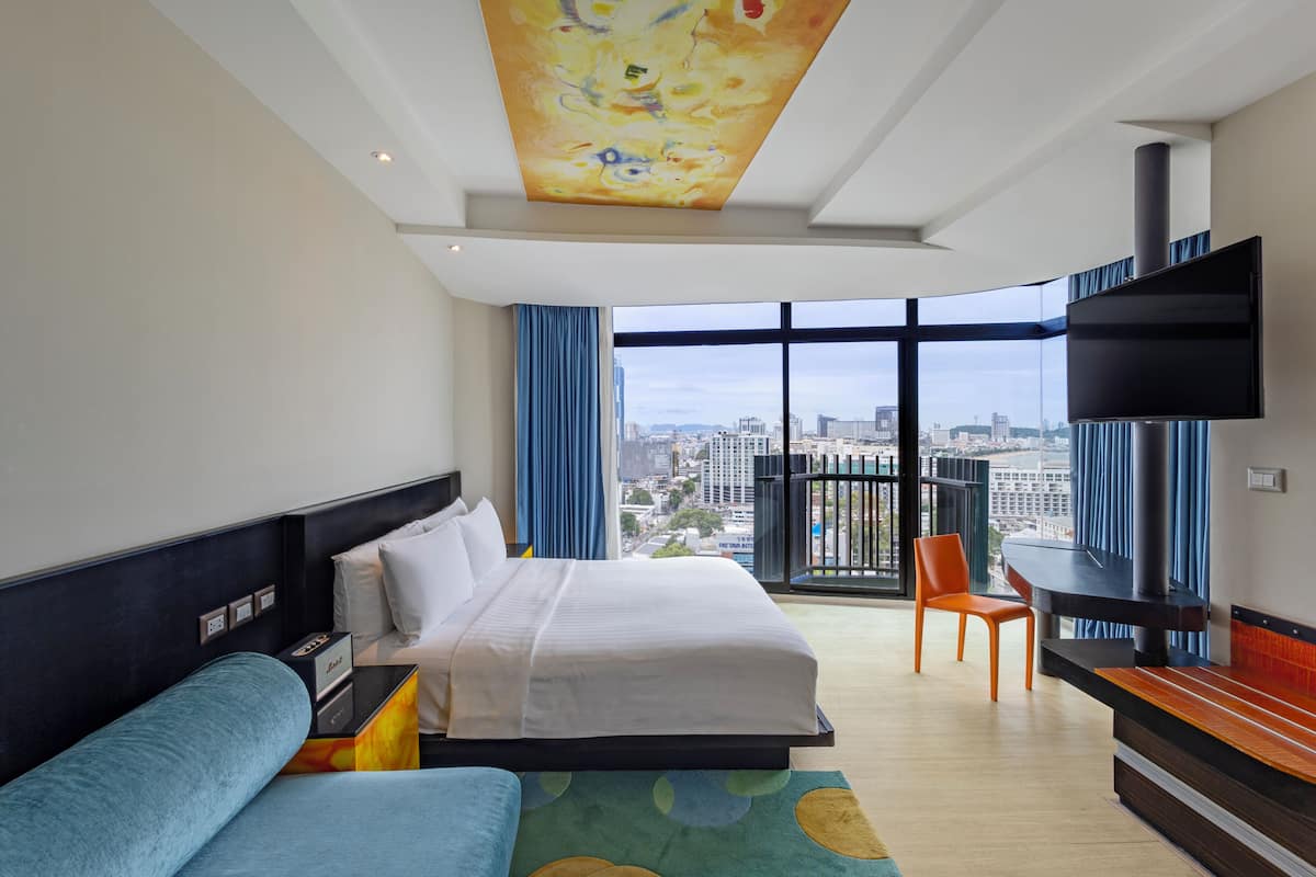 Habitación de hotel con una cama grande, un escritorio, una silla, un televisor y vistas a la ciudad.