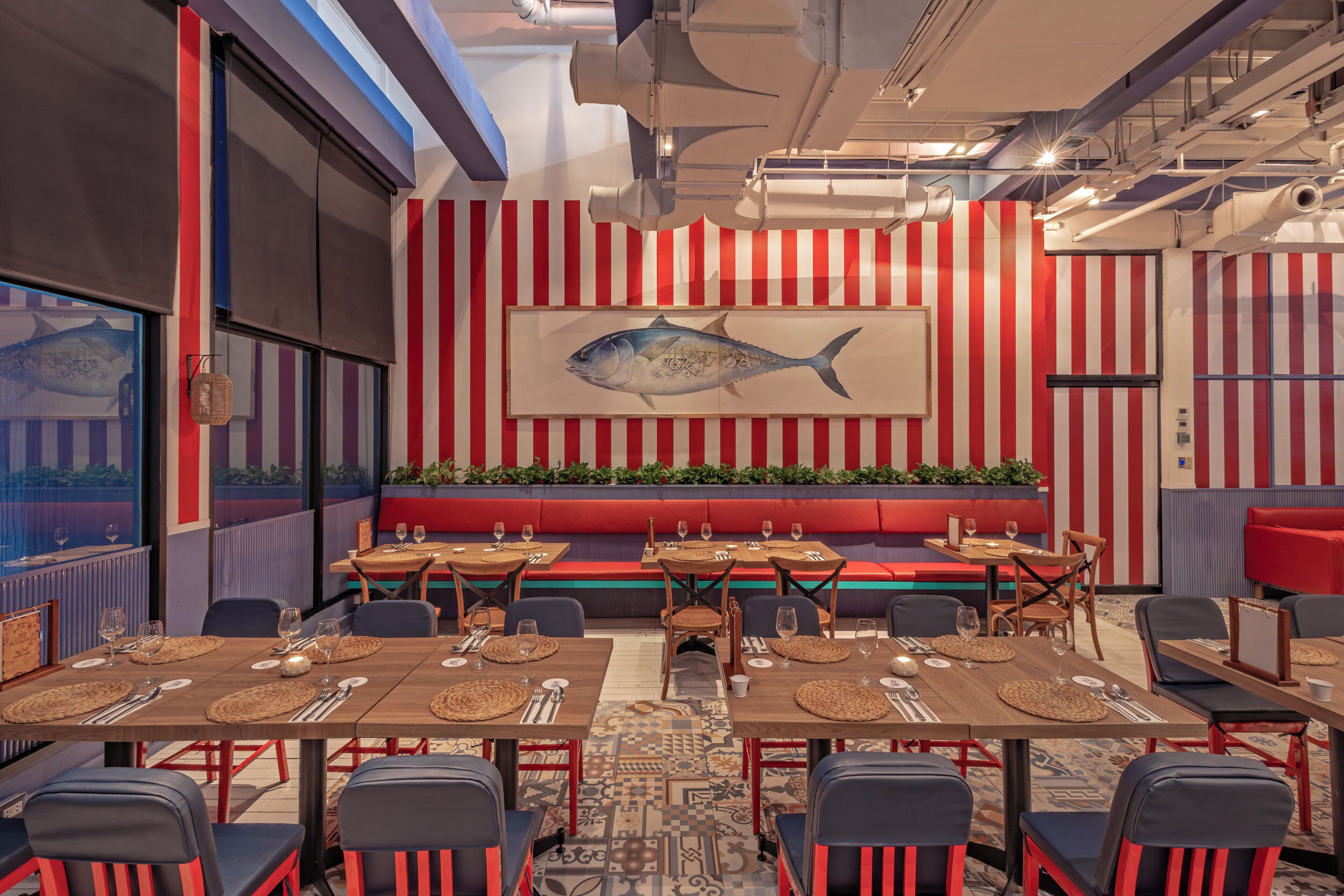 A restaurant interior with striped walls, a large fish mural, and a mix of red and blue seating.