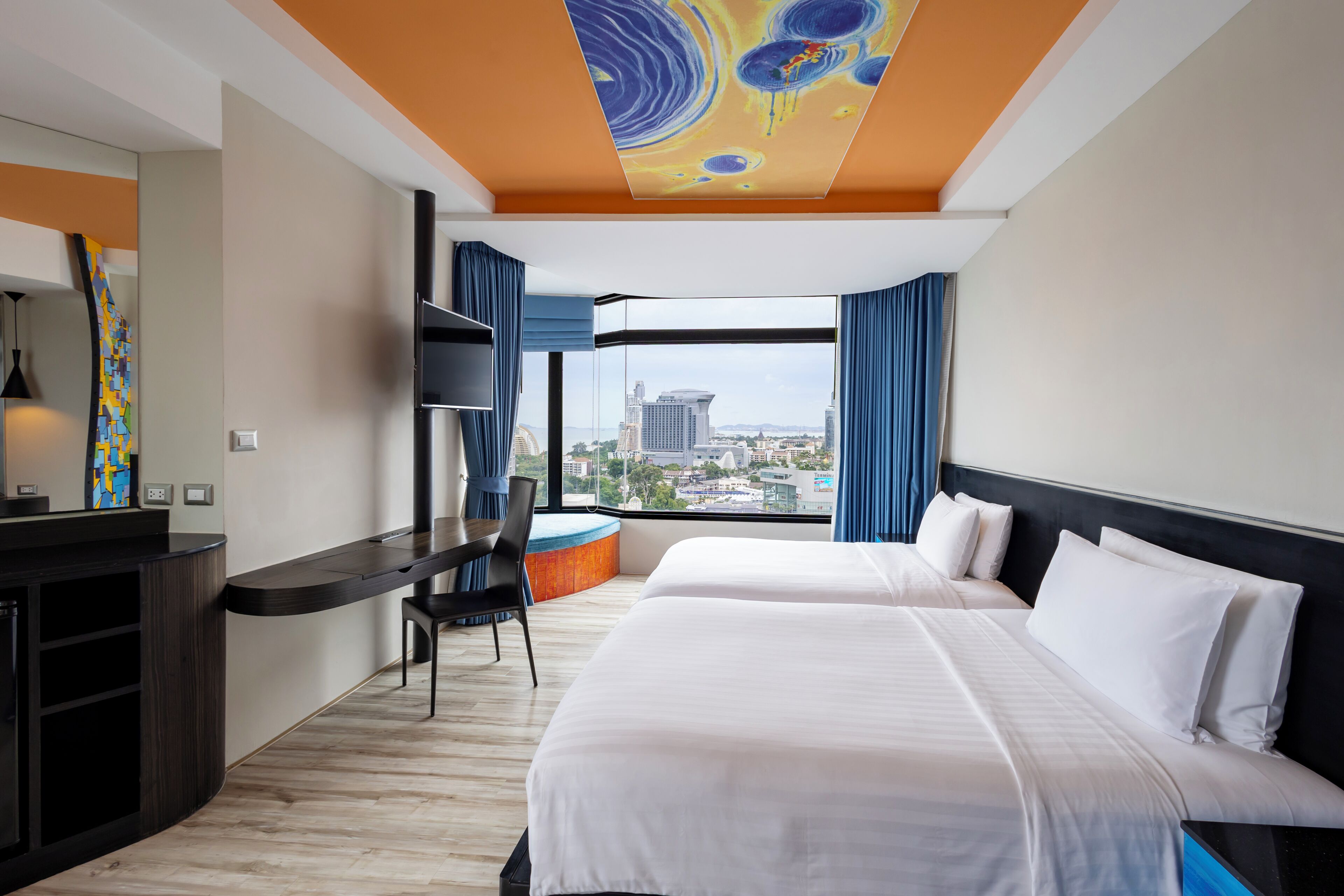 A hotel room with a large bed, a desk, a chair, and a city view.
