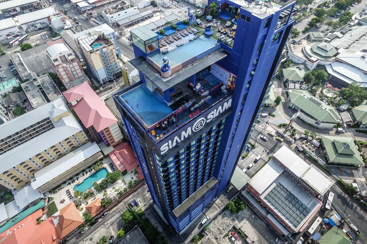 A high-rise building with a prominent 'SIAM' sign, surrounded by other buildings and a pool area.