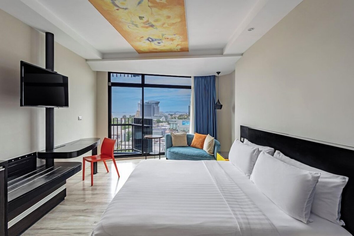 A hotel room with a bed, a TV, a desk, and a view of the city.