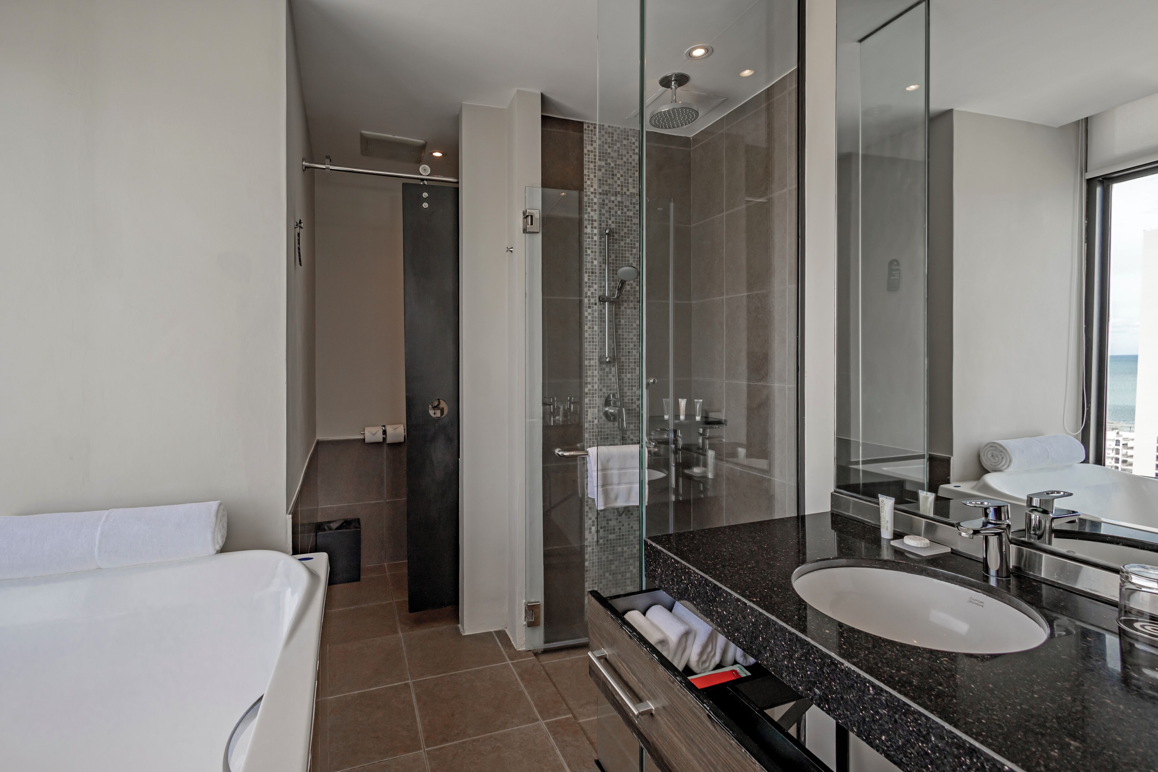 Un baño moderno con ducha de vidrio, un espejo grande y un lavamanos blanco.