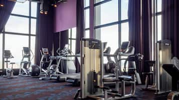 A gym with various exercise machines, large windows, and purple walls.