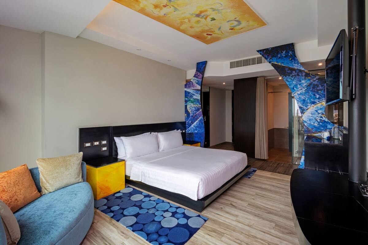 Una habitación de hotel moderna con una cama grande, un sofá, un televisor y un diseño de techo original.