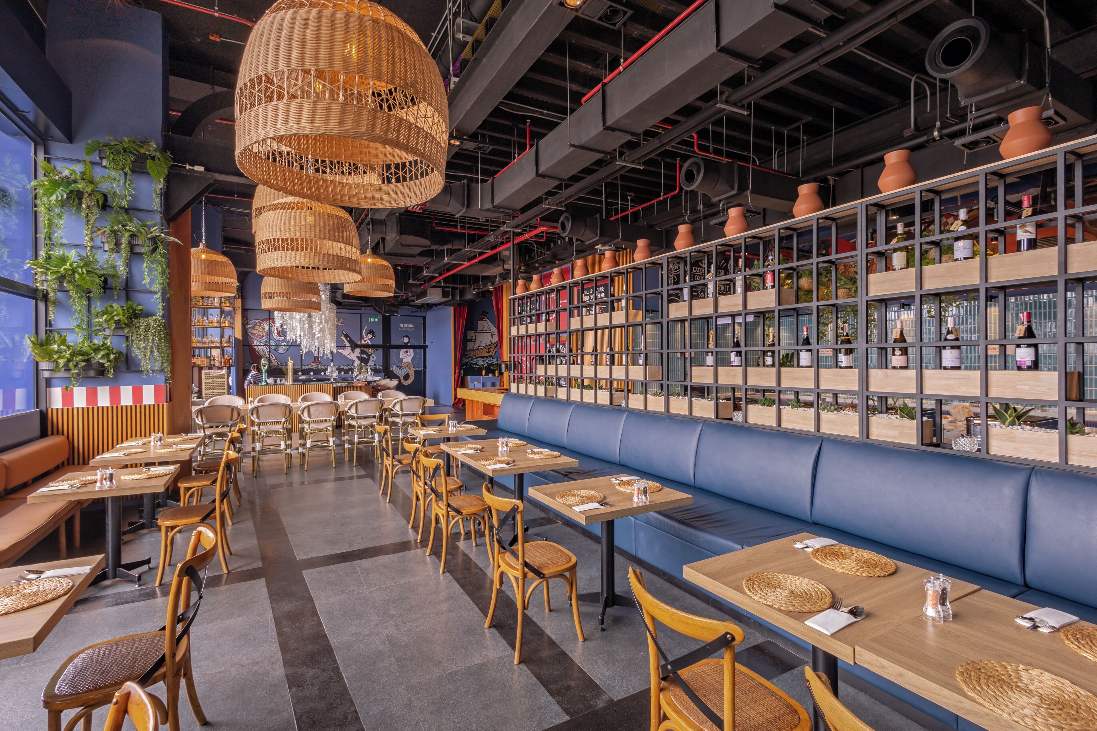 A restaurant interior with high ceilings, exposed pipes, and a variety of seating options including tables and benches.