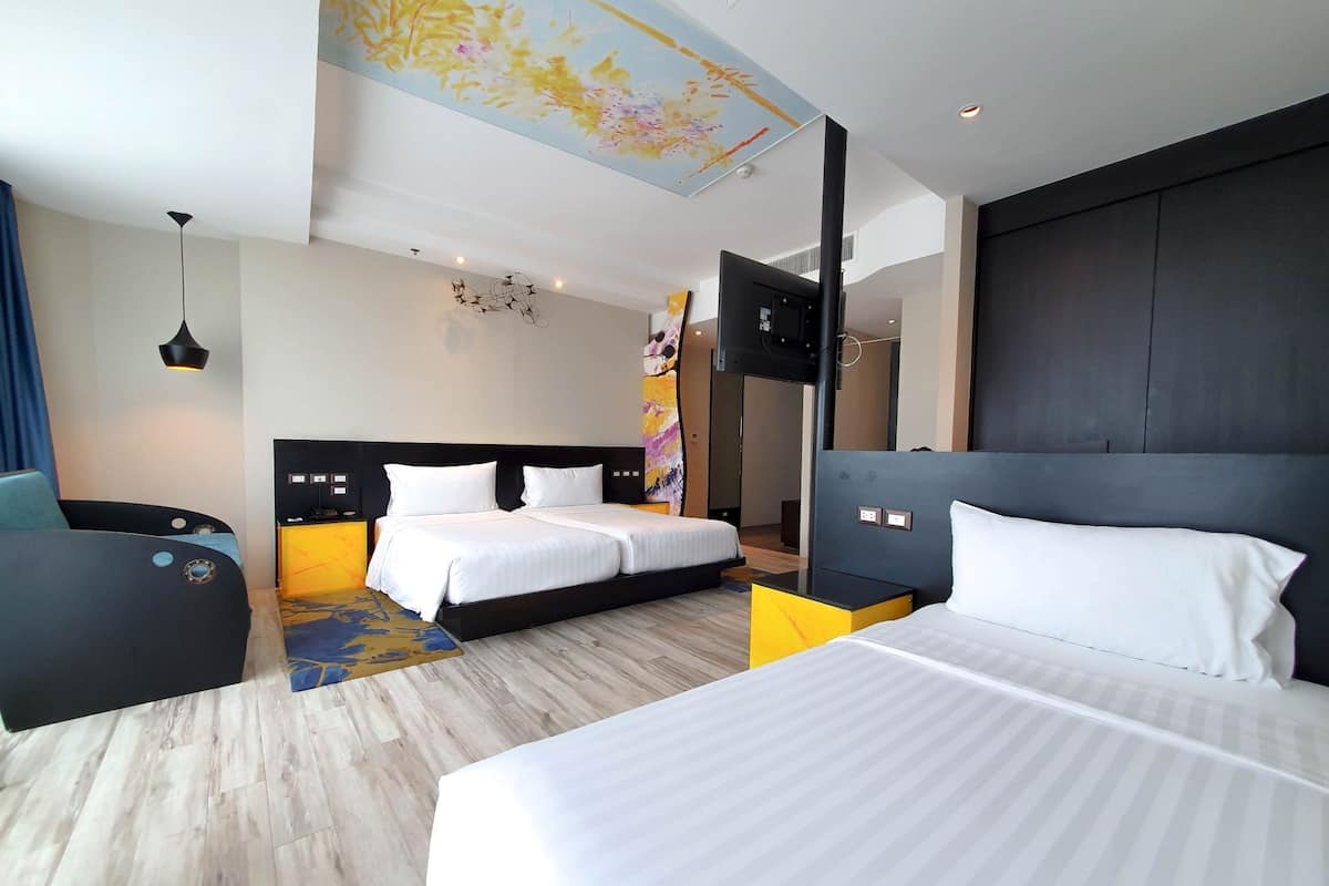 Habitación de hotel con dos camas, un escritorio, una silla, un televisor y una obra de arte en el techo.