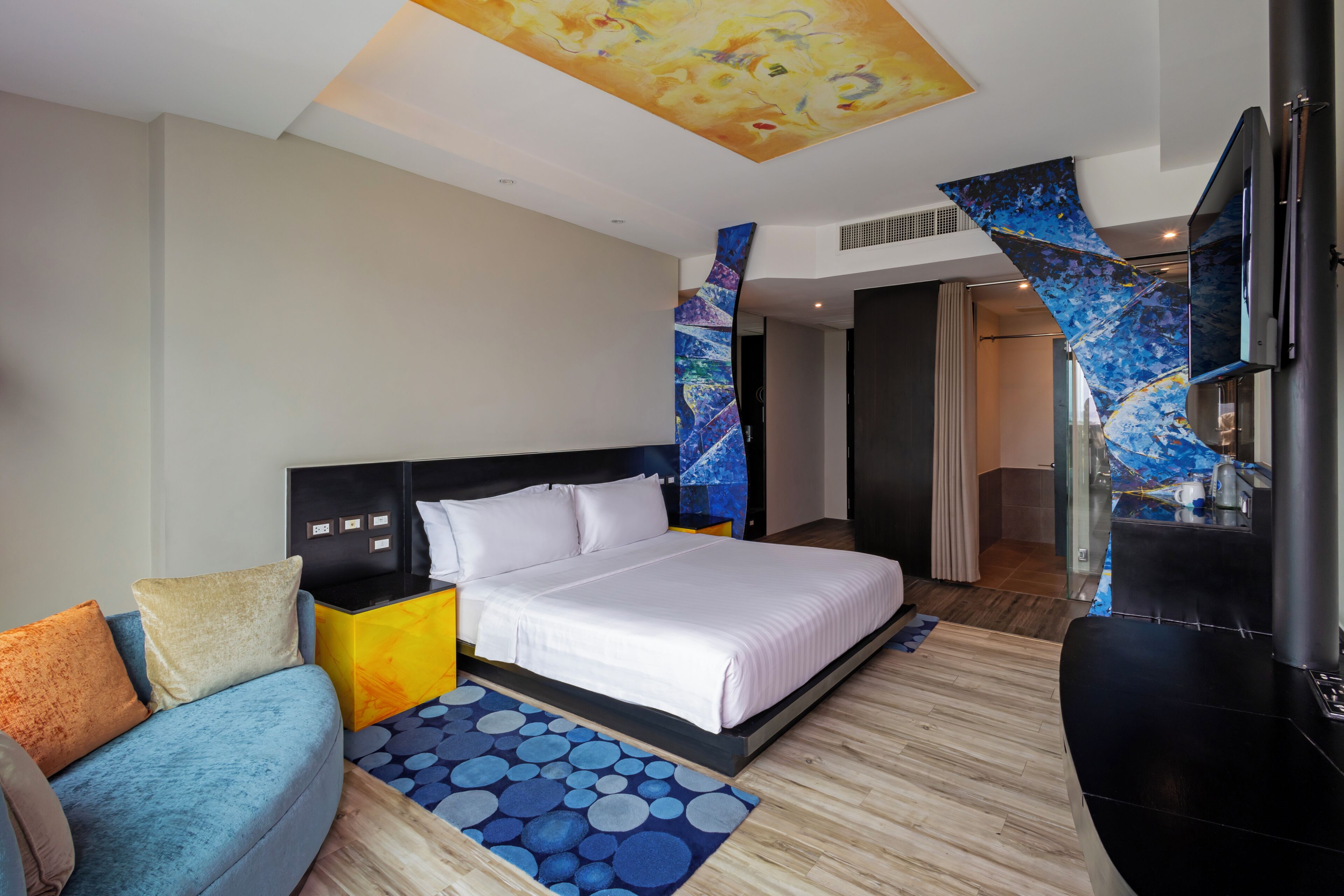 Ein modernes Hotelzimmer mit Bett, Sofa, Fernseher und einem außergewöhnlichen Deckenstil.