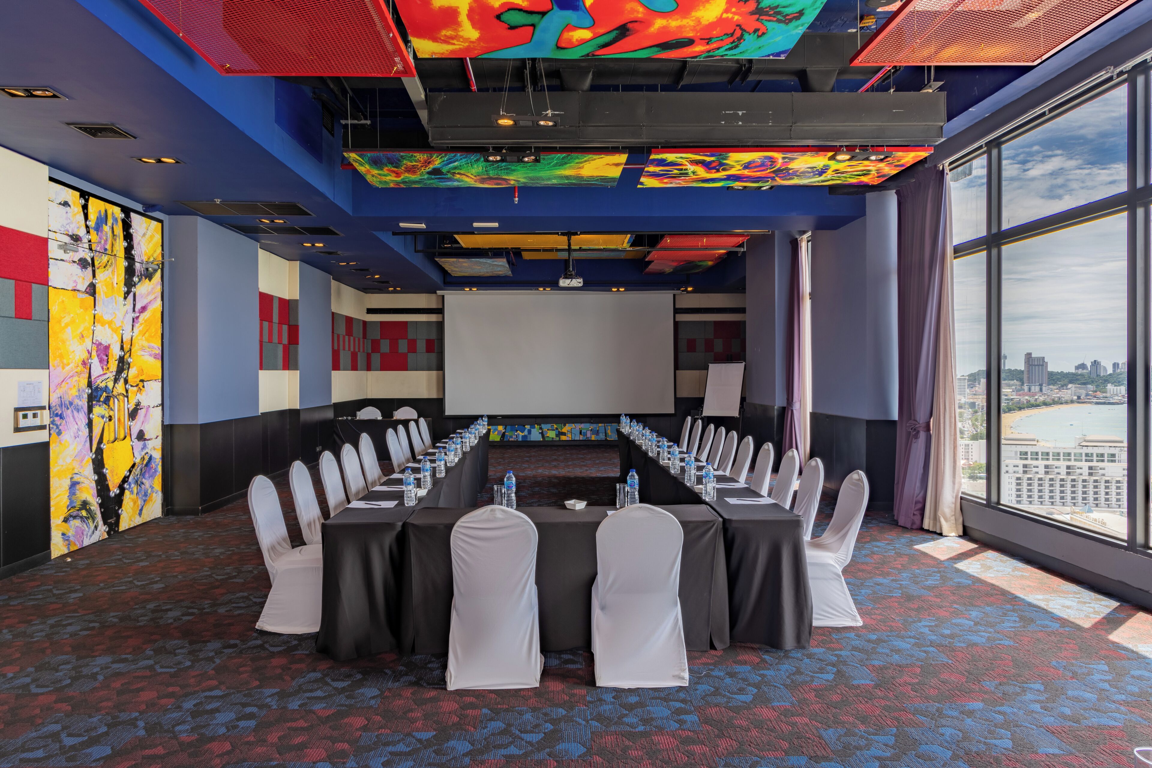 A conference room with a long table, chairs, and a projector screen.