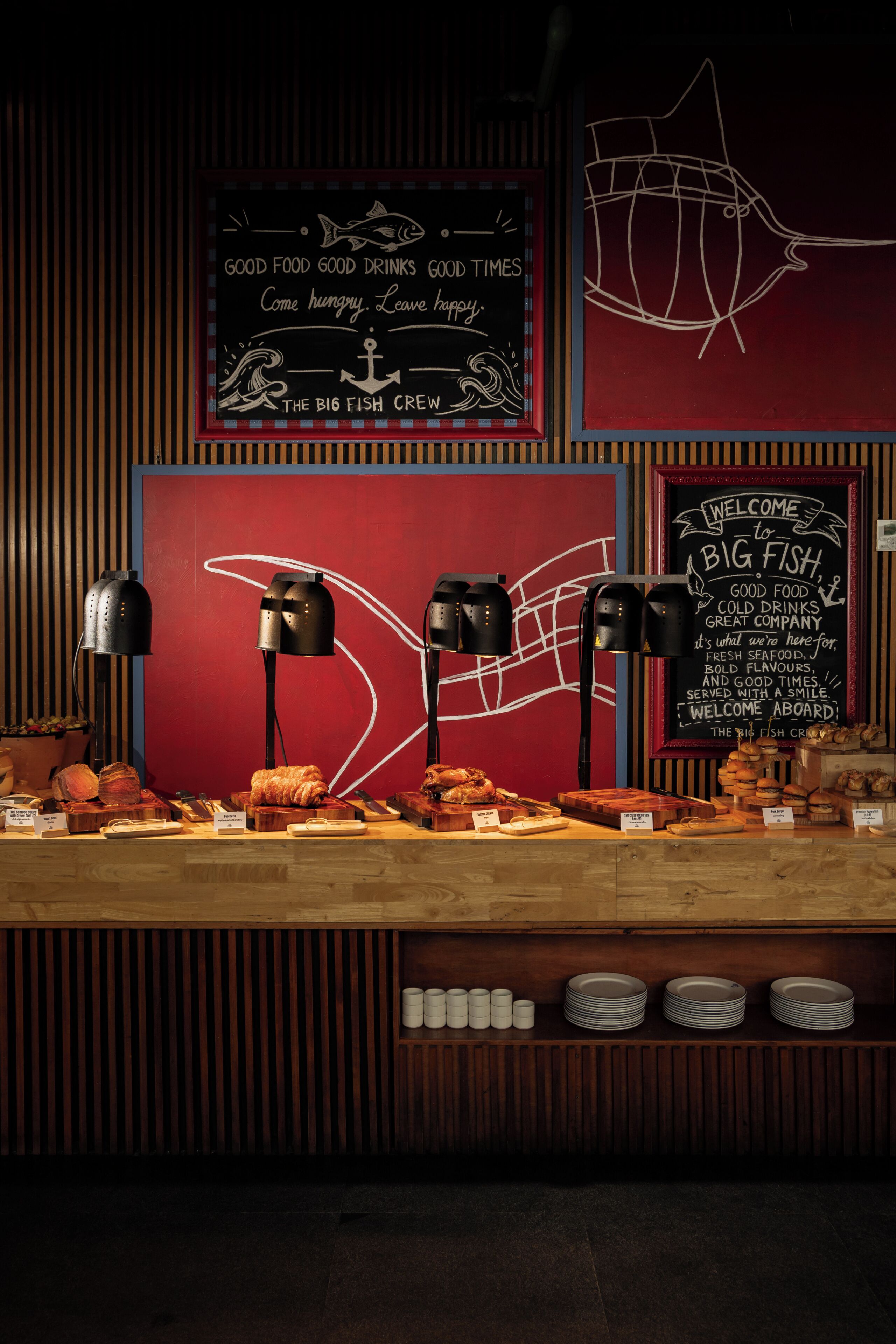 A restaurant counter with seafood dishes, a chalkboard menu, and a welcome sign.