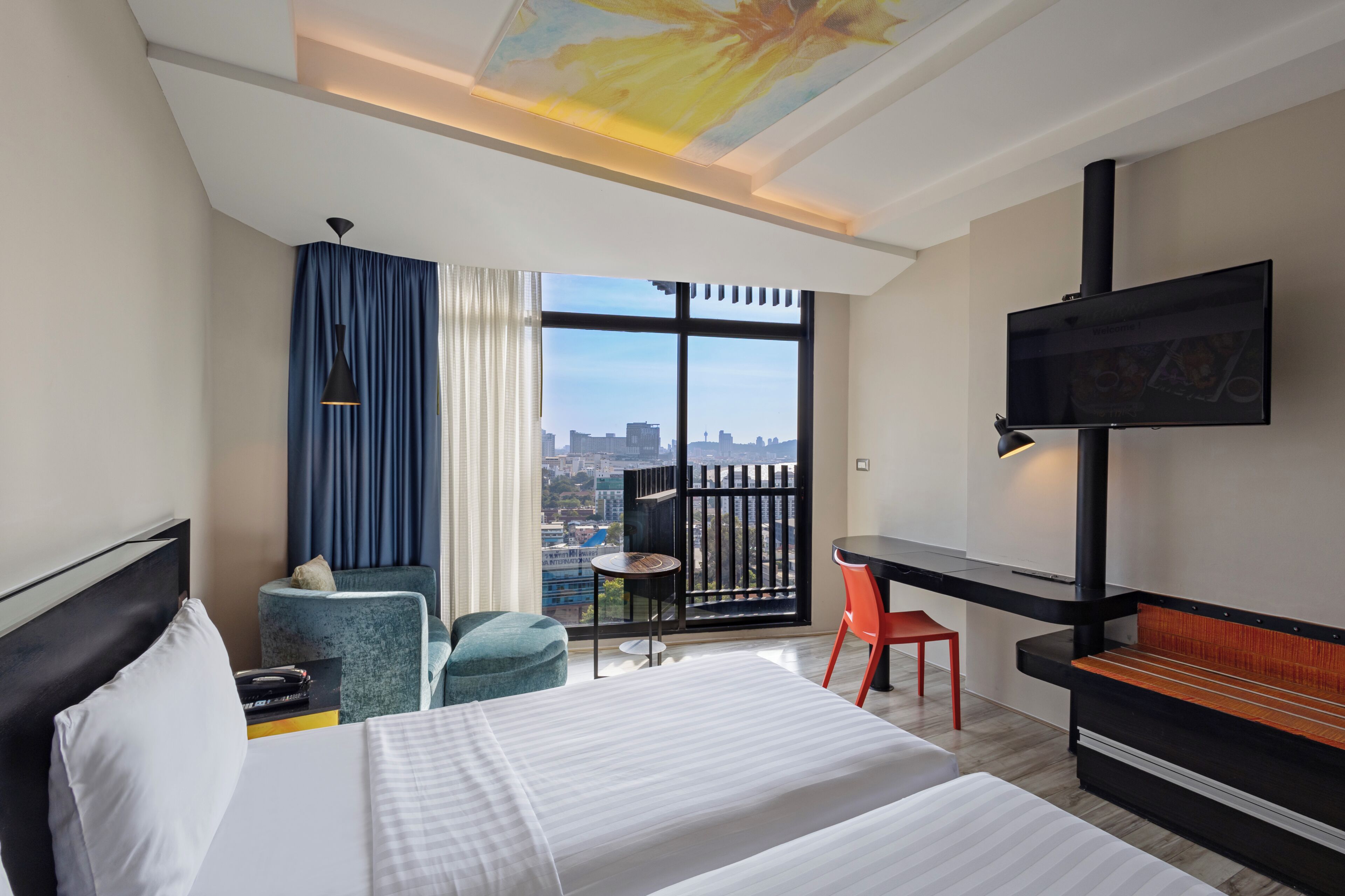 A hotel room with a bed, a desk, a TV, a chair, a small table, and a view of the city.