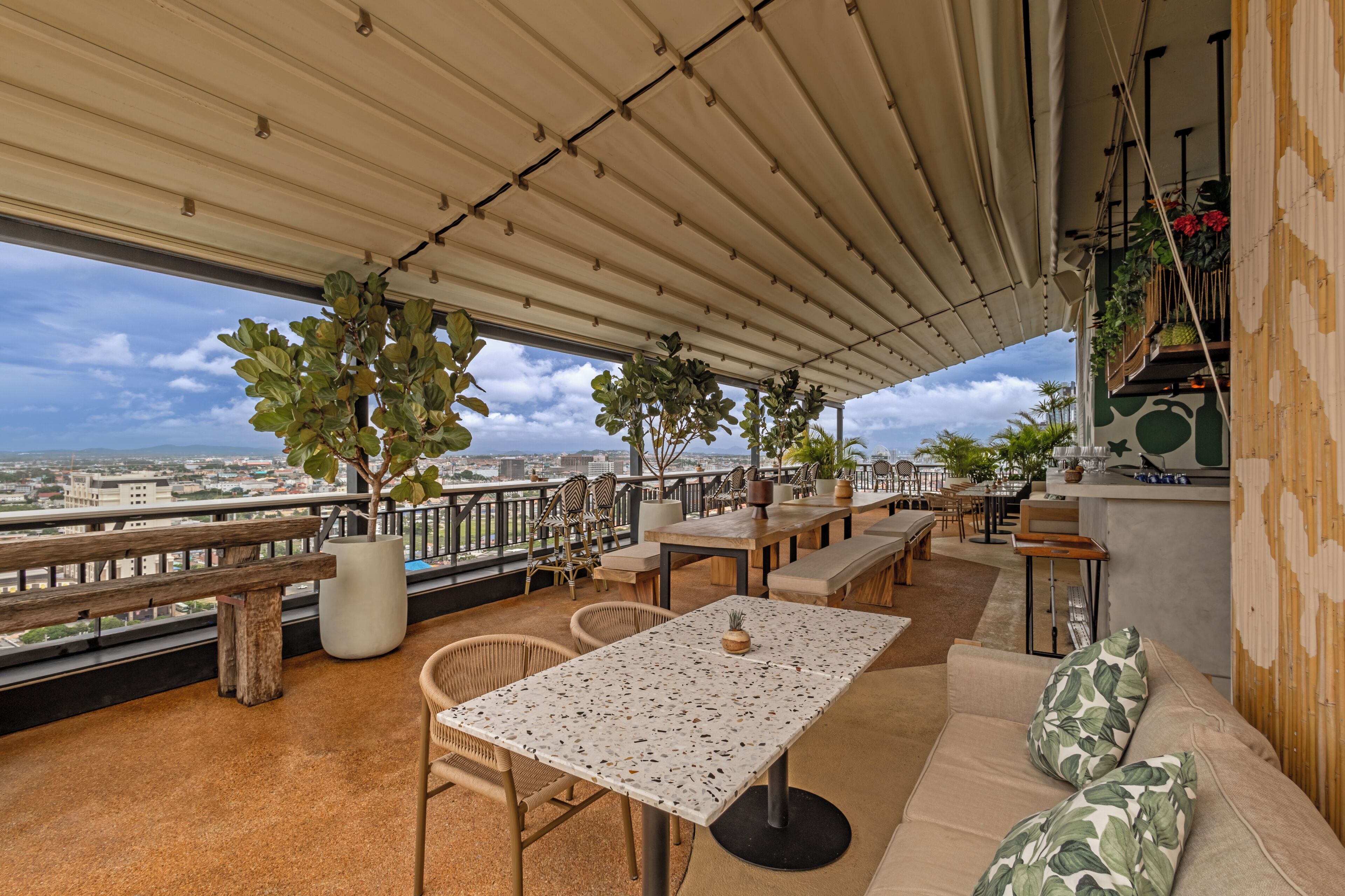 An outdoor terrace with a view of the city, furnished with tables, chairs, and a sofa.