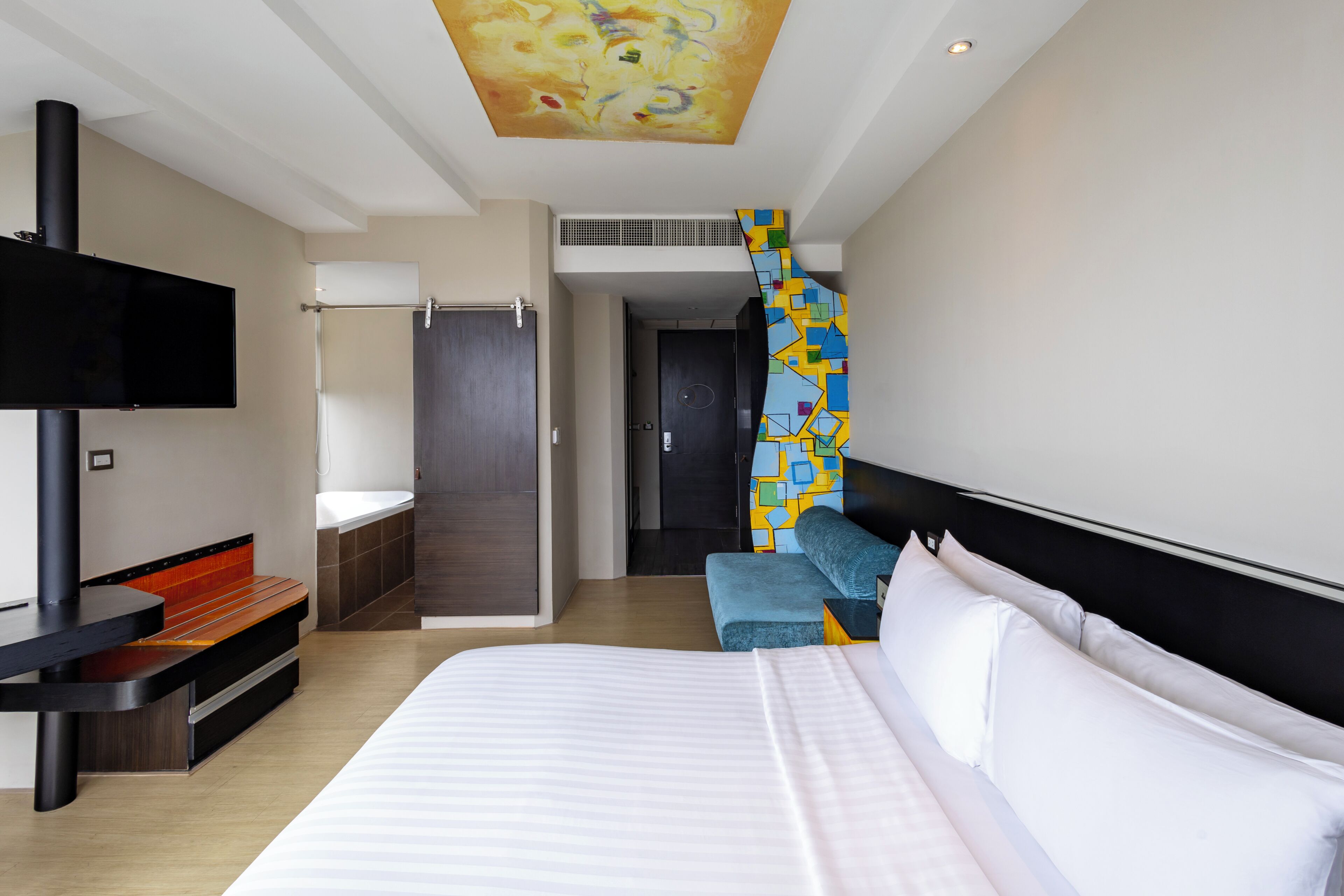 A modern hotel room with a bed, a TV, a desk, a sofa, and a staircase leading to a bathroom.