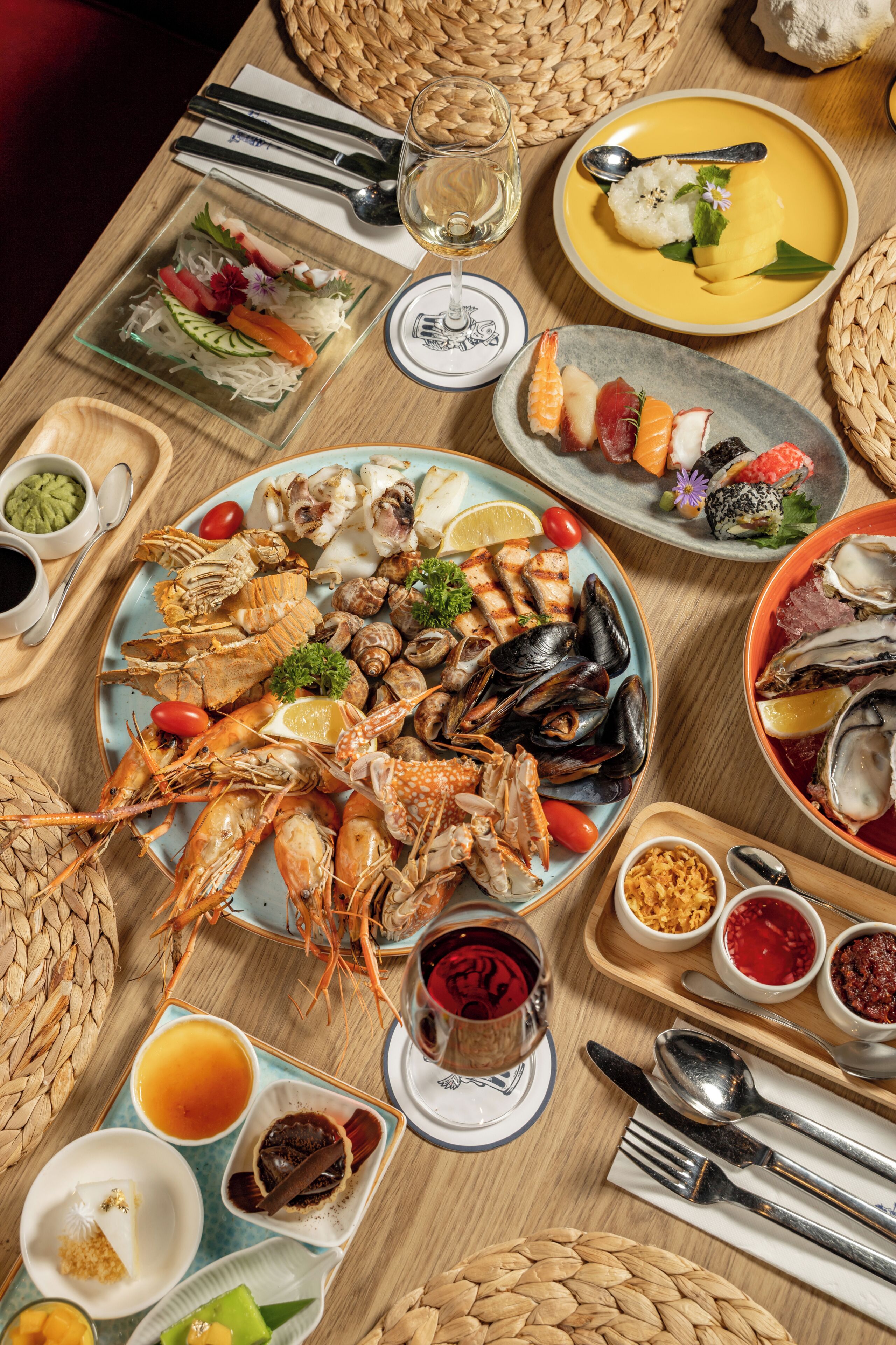 A table set with various seafood dishes, including shrimp, mussels, and oysters, accompanied by condiments and drinks.