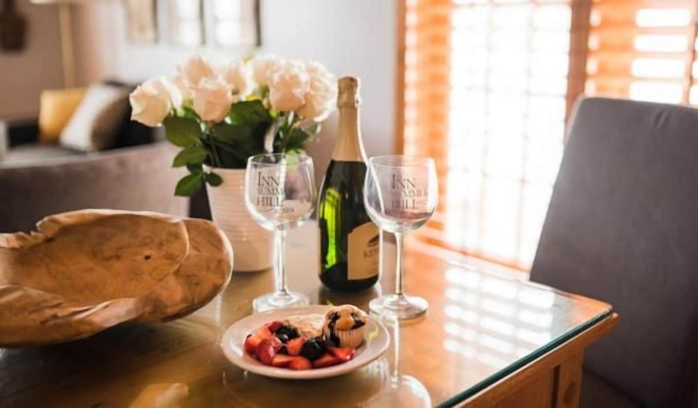 A table with a bottle of champagne, two glasses, a plate of fruit, and a vase of flowers.