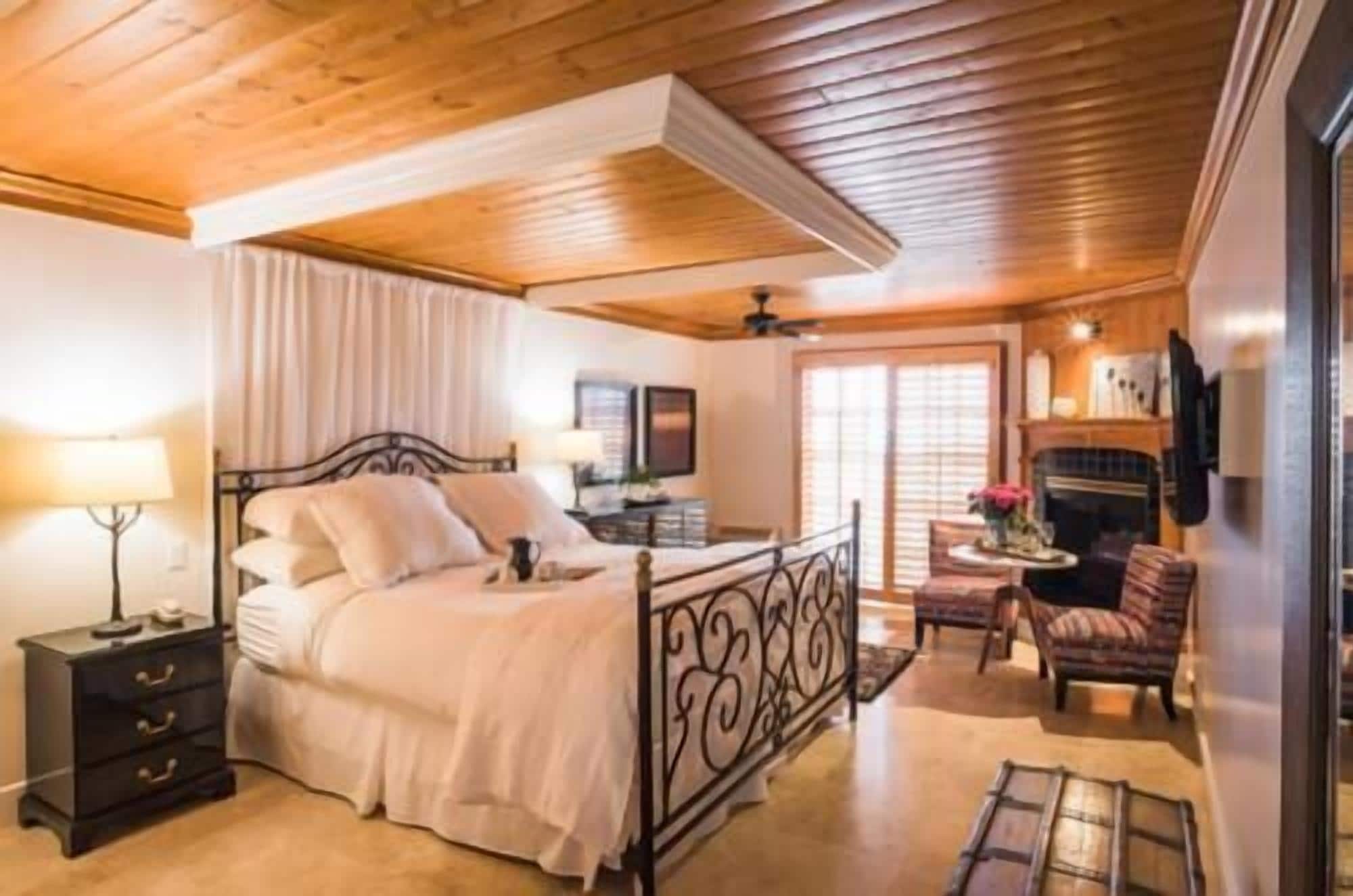 Een slaapkamer met een houten plafond, een bed met hoofdbord, een nachtkastje, een stoel en een open haard.