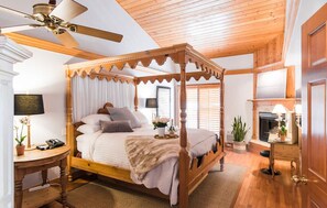 A four-poster bed with a canopy, a wooden ceiling fan, a bedside table with a lamp, and a fireplace in the background. - Inn on Summer Hill (Santa Barbara)