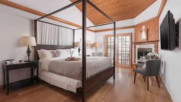 A four-poster bed with a wooden ceiling, a small table with a chair, and a fireplace.
