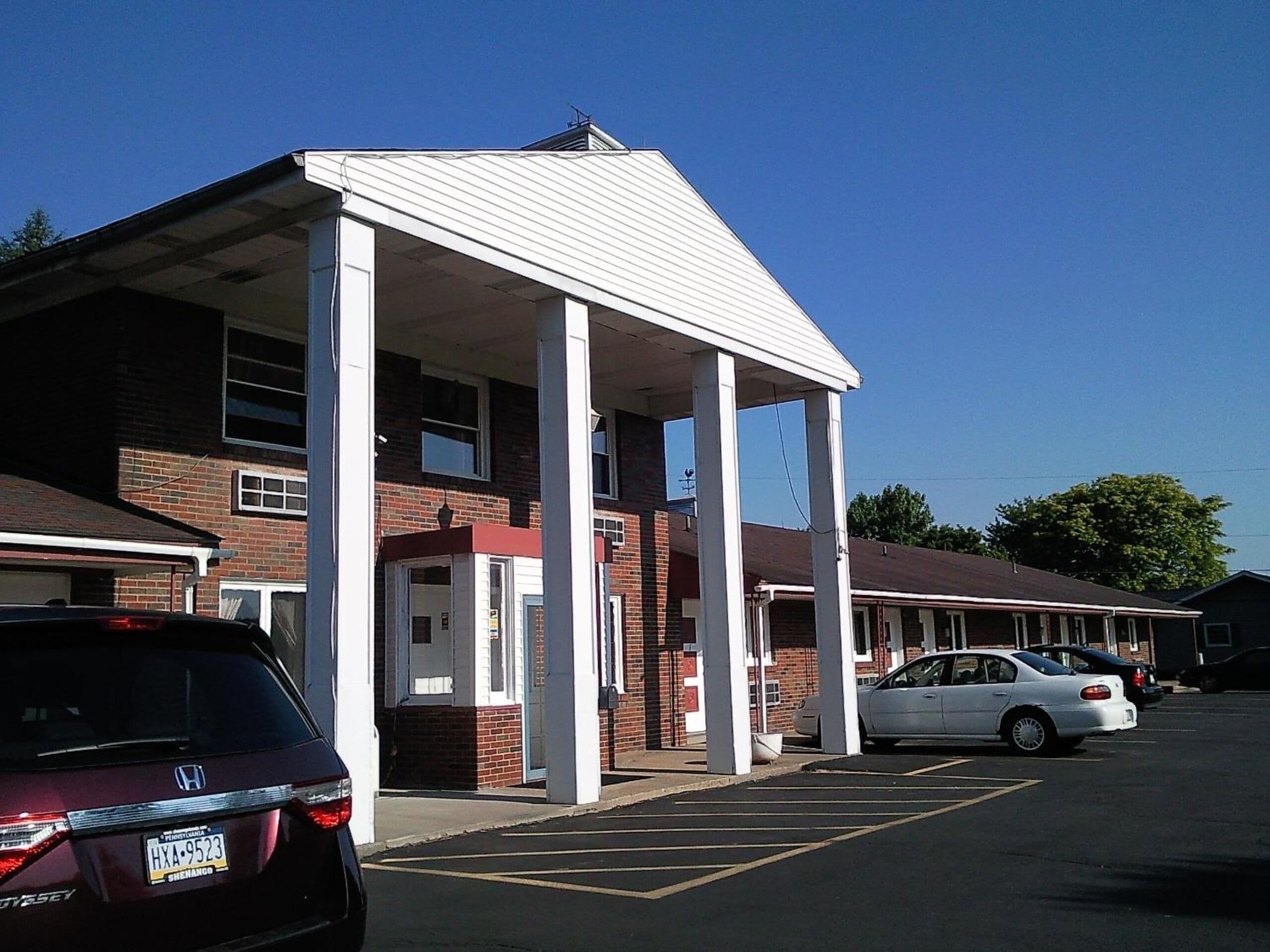 A motel with a covered entrance, brick exterior, and a parking lot with several cars.