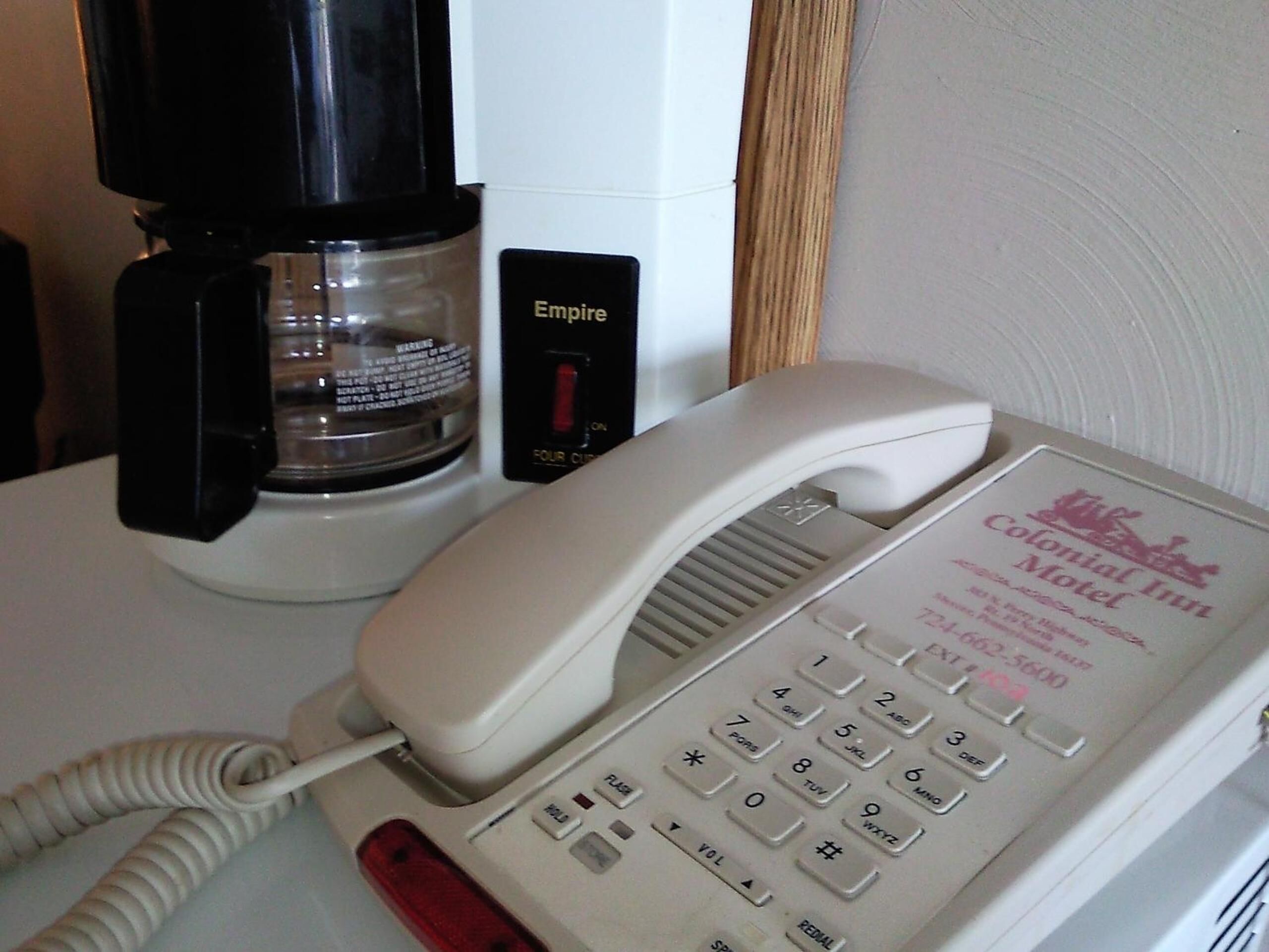 A white telephone with a red handset, a black coffee maker, and a sign for the Colonial Inn Motel.
