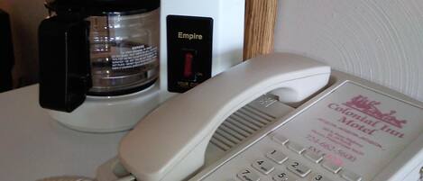 A white telephone with a red handset, a black coffee maker, and a sign for the Colonial Inn Motel.