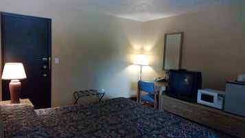 Een hotelkamer met een bed, een bureau met een lamp, een televisie en een magnetron.