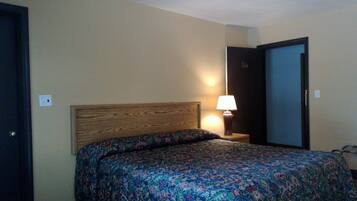 A hotel room with a wooden headboard, a patterned bedspread, a bedside lamp, and a door with a number on it.