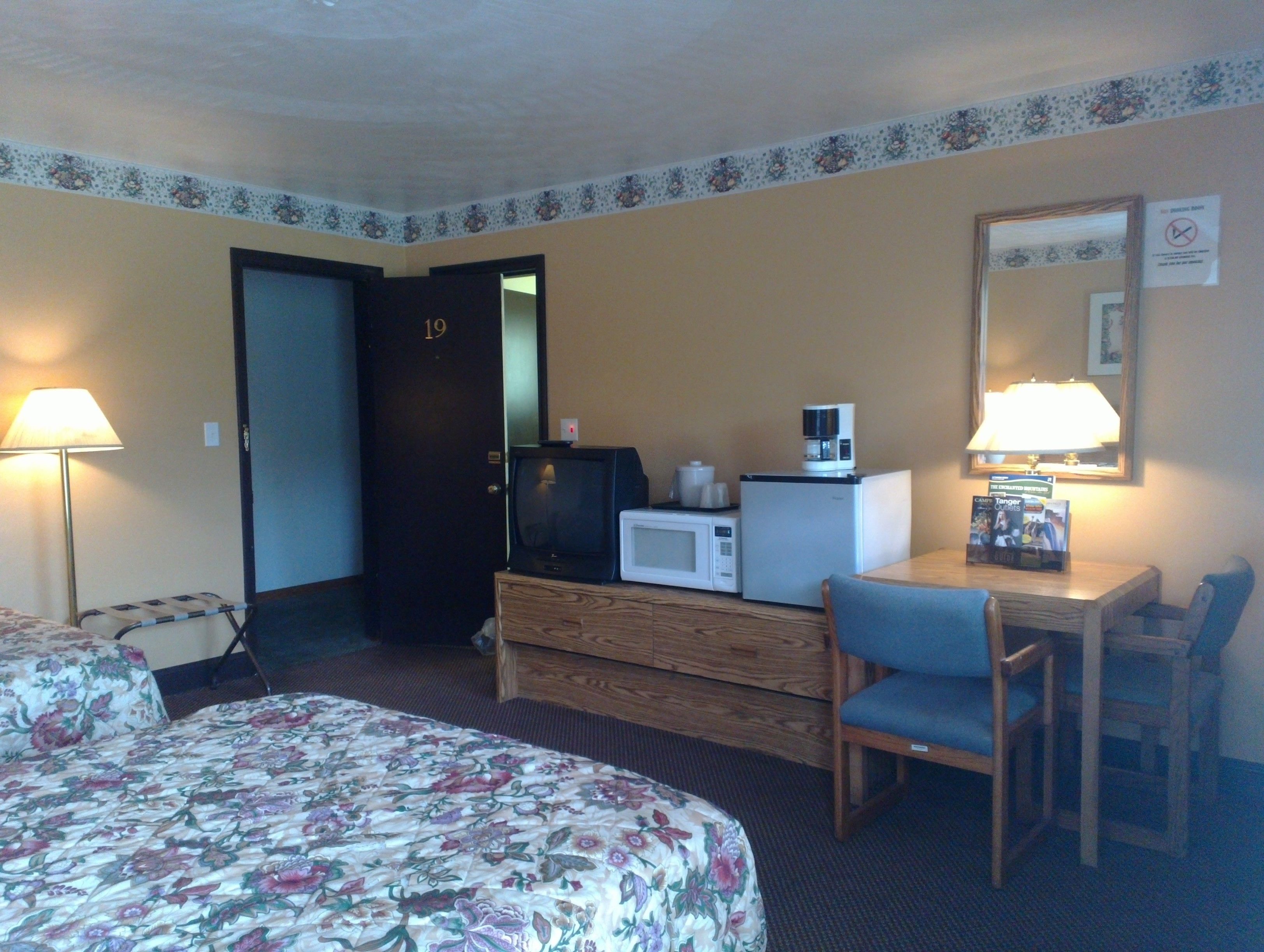 A hotel room with a bed, a desk with a chair, a microwave, a television, and a door marked with the number 19.